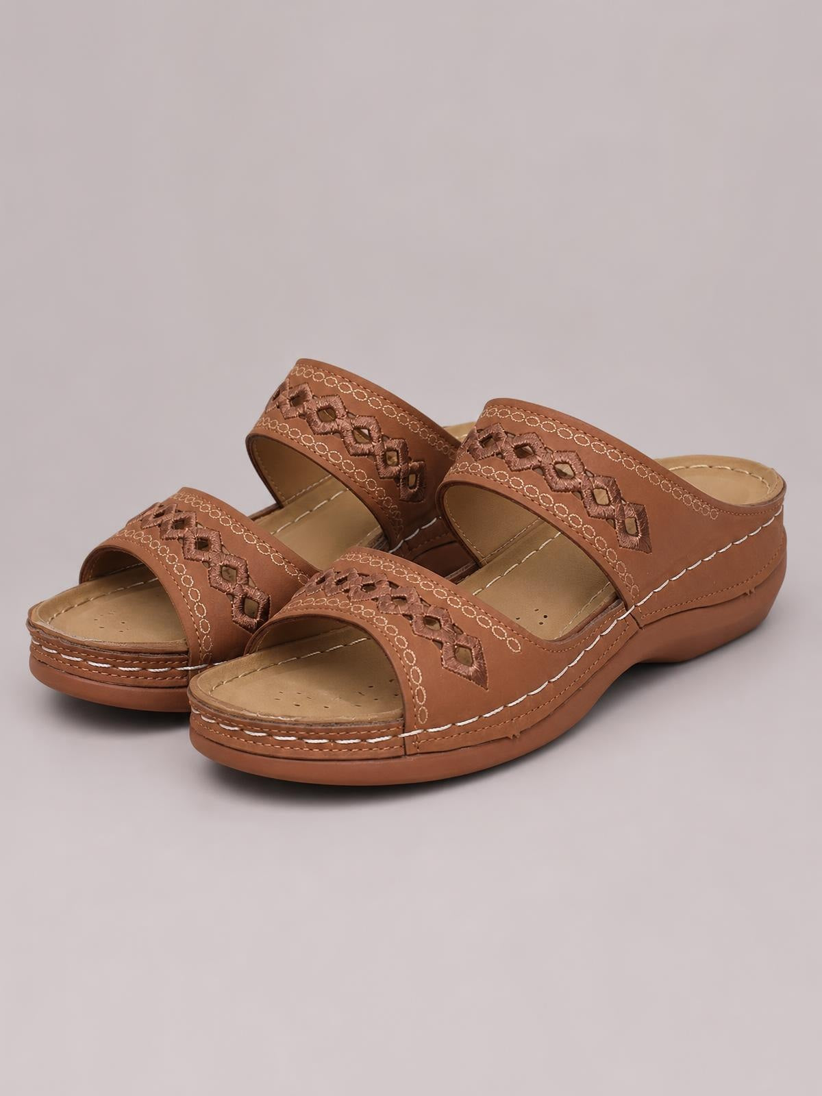Brown open-toe flat sandals feature wide PU leather straps with decorative geometric stitching, cushioned footbeds, and durable rubber soles.