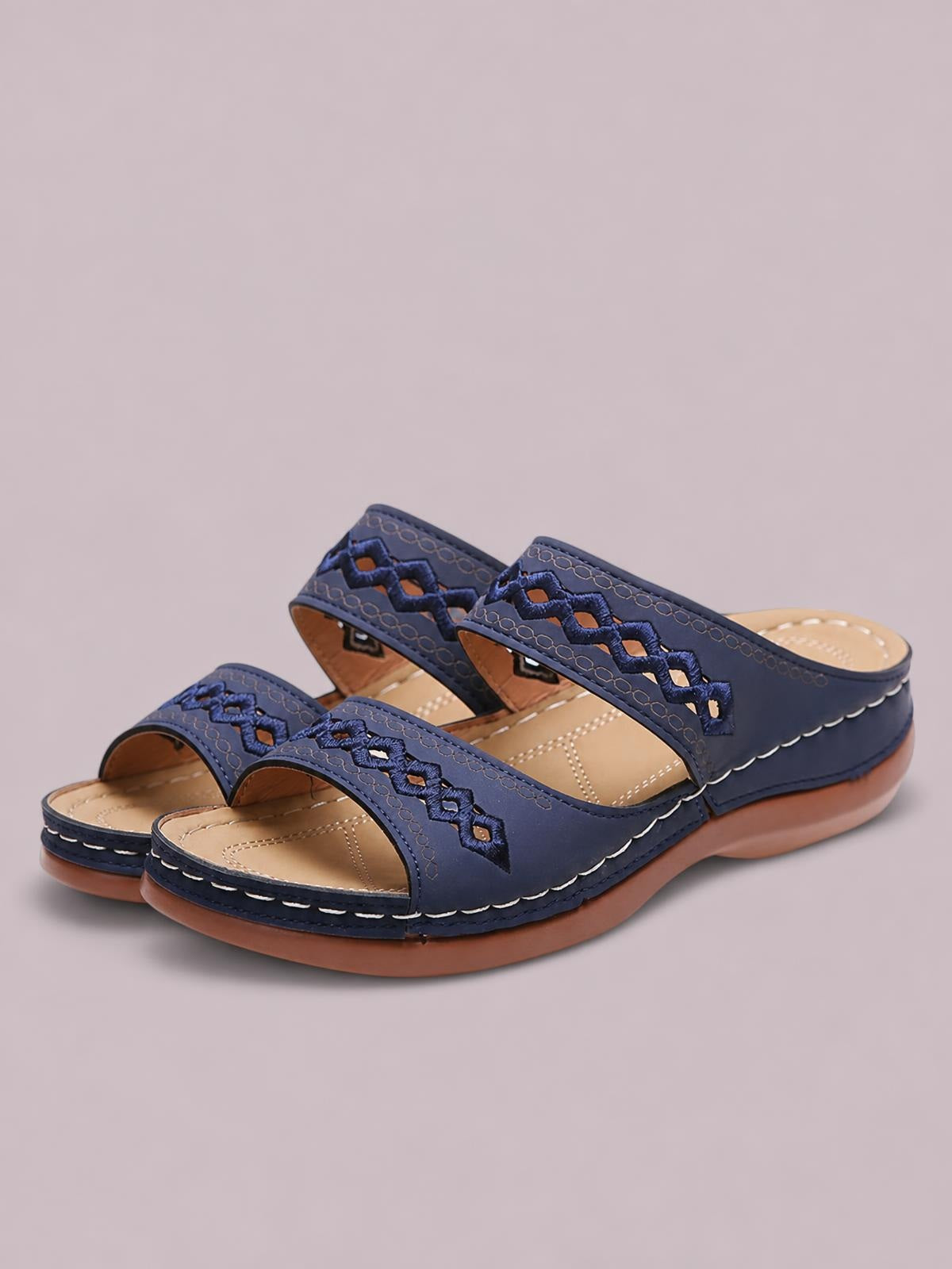 Navy blue open toe flat sandals feature crisscross cutout straps, tan cushioned footbeds, white stitching, and sturdy brown rubber soles.