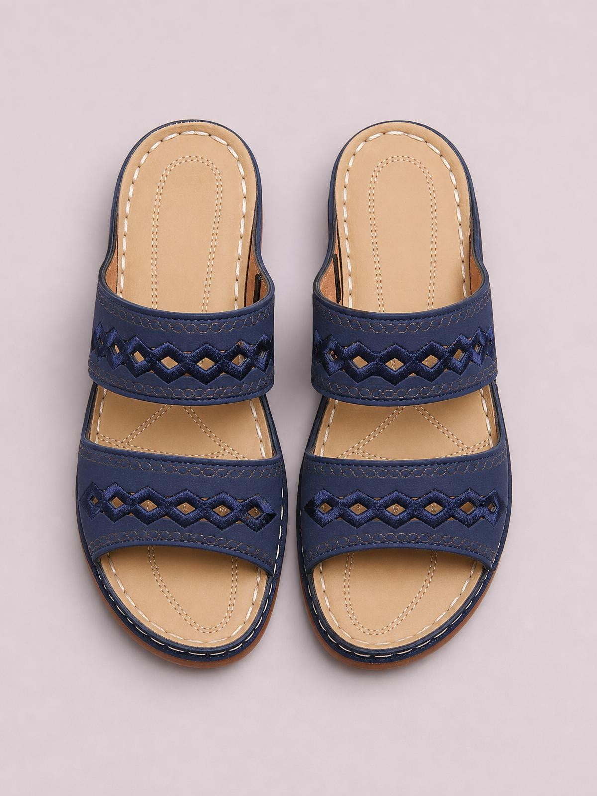 Pair of navy blue open-toe flat sandals in PU leather, featuring two wide geometric cutout straps, tan stitched insoles, and low rubber soles.