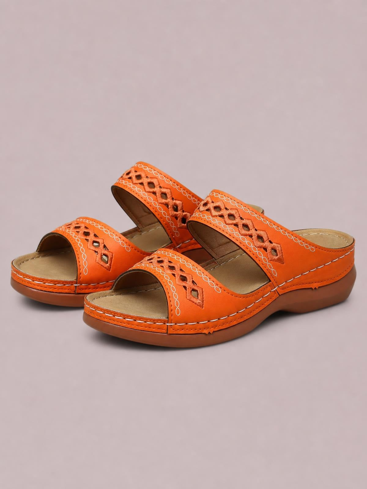 Orange open-toe flat sandals feature wide decorative cutout straps, contrast stitching, cushioned footbeds, and sturdy low rubber soles.