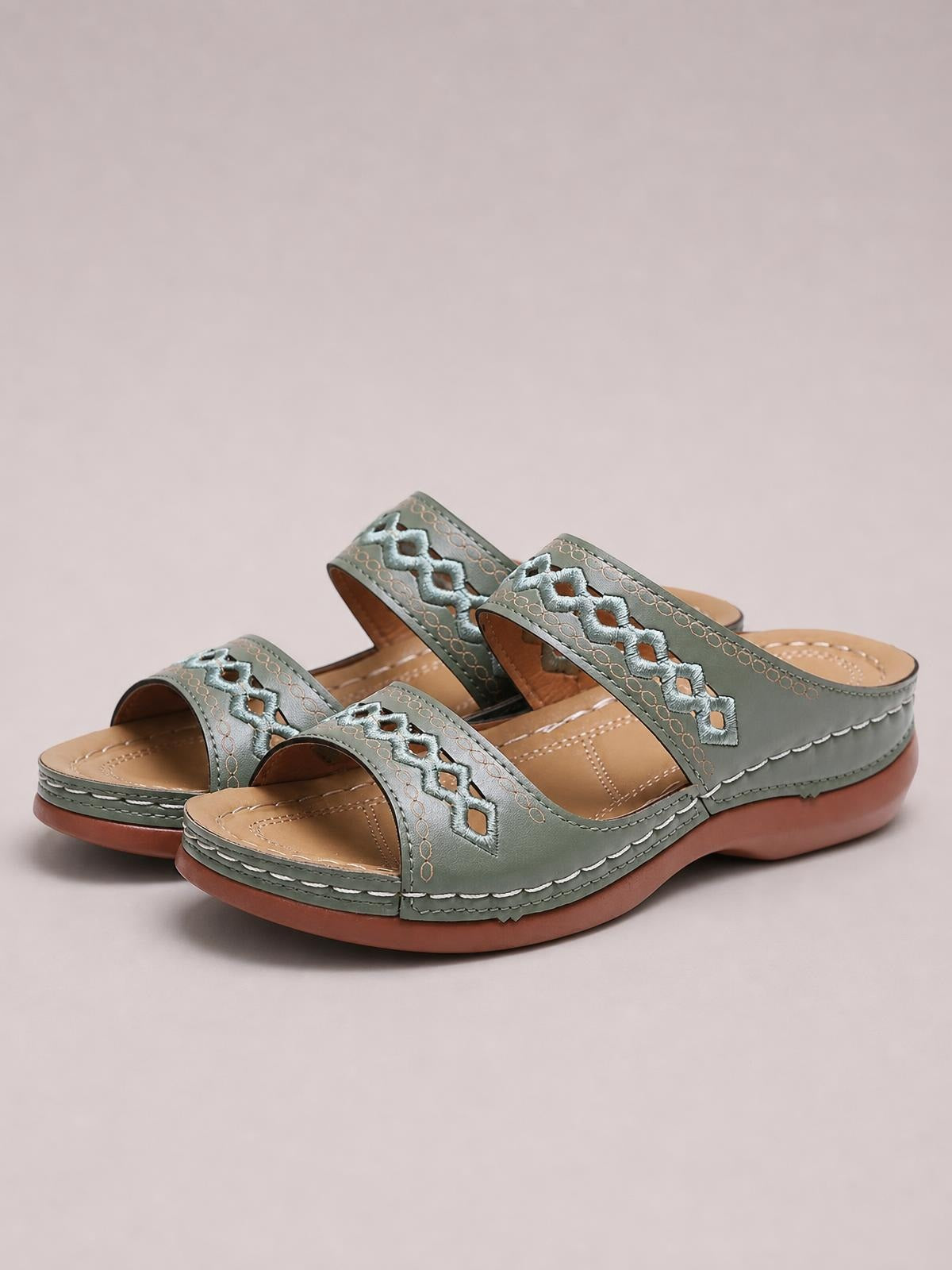 Sage green open toe flat sandals feature wide embroidered straps, stitched PU leather construction, cushioned tan footbeds, and low rubber soles.