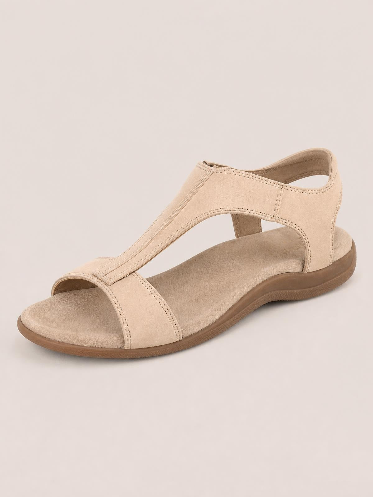 Beige open-toe flat sandal in PU leather with a wide toe strap, stitched T-strap construction, cushioned footbed, and flexible rubber sole.