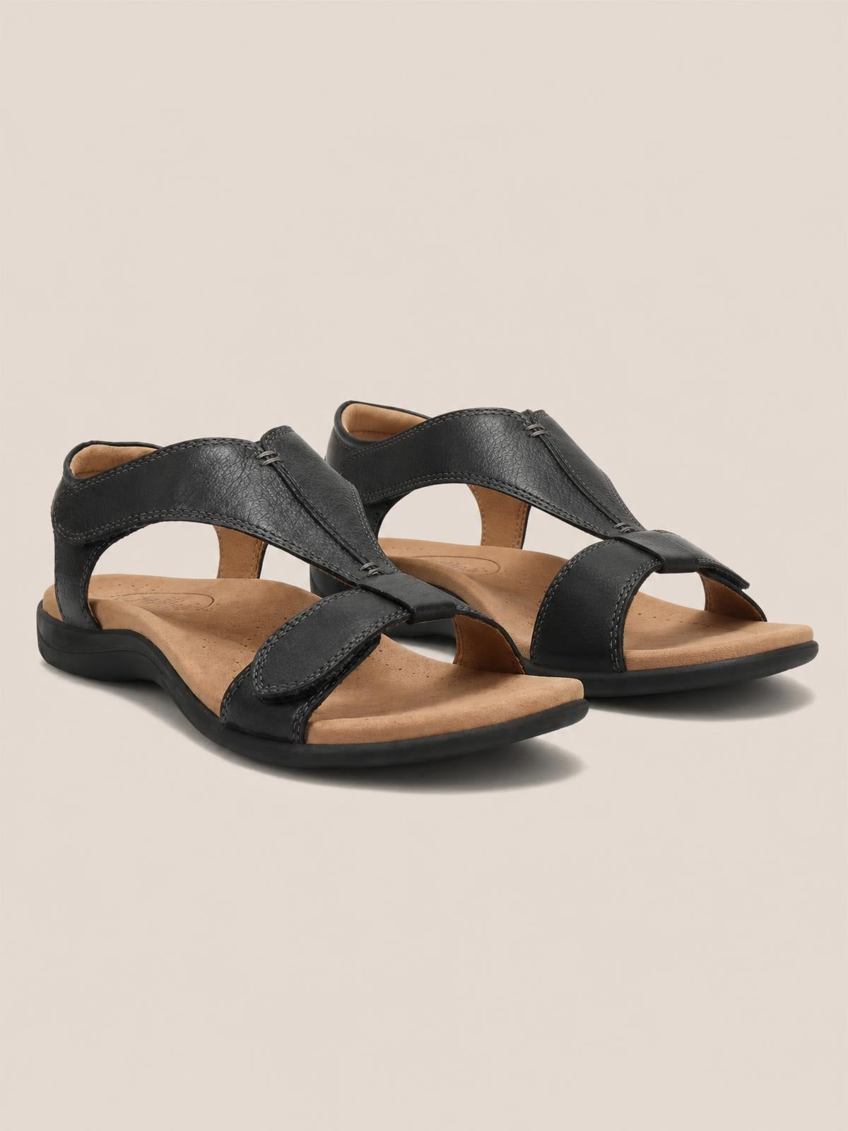 Black open-toe flat sandals with wide stitched crossover straps, adjustable buckle closures, tan cushioned footbeds, and flexible rubber soles.