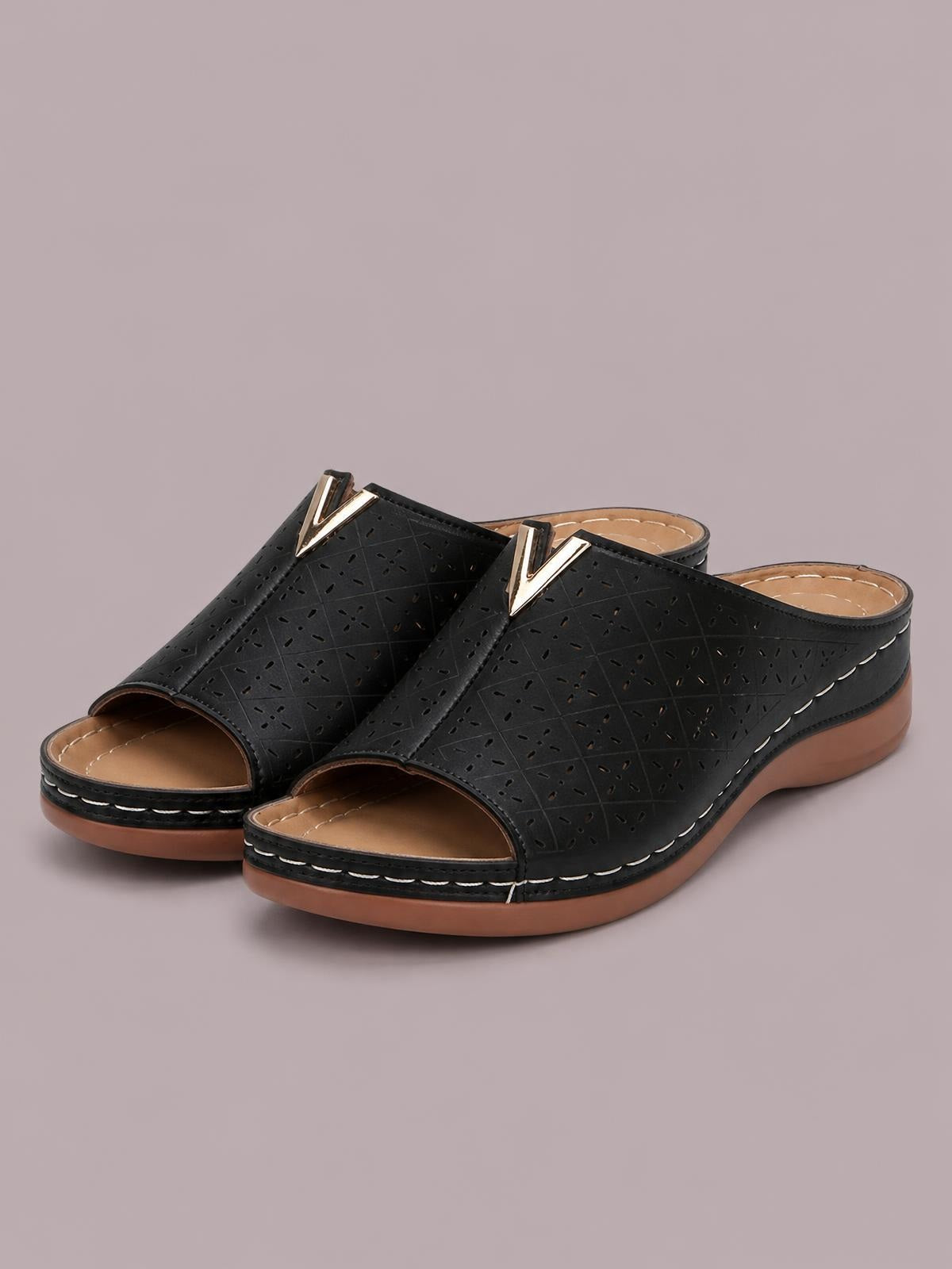 Black open-toe flat mule sandals in PU leather feature perforated geometric uppers, gold V embellishments, tan footbeds, and brown rubber soles with stitched trim.