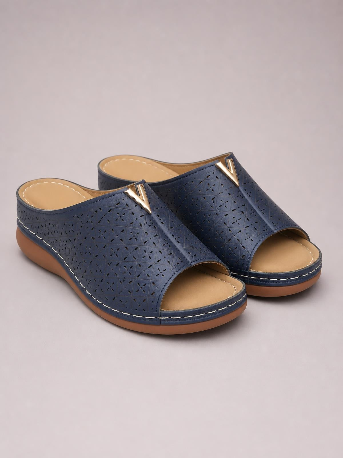 Navy blue open toe flat sandals in perforated PU leather feature wide vamp straps, metallic V accents, tan footbeds, and contrasting rubber soles.