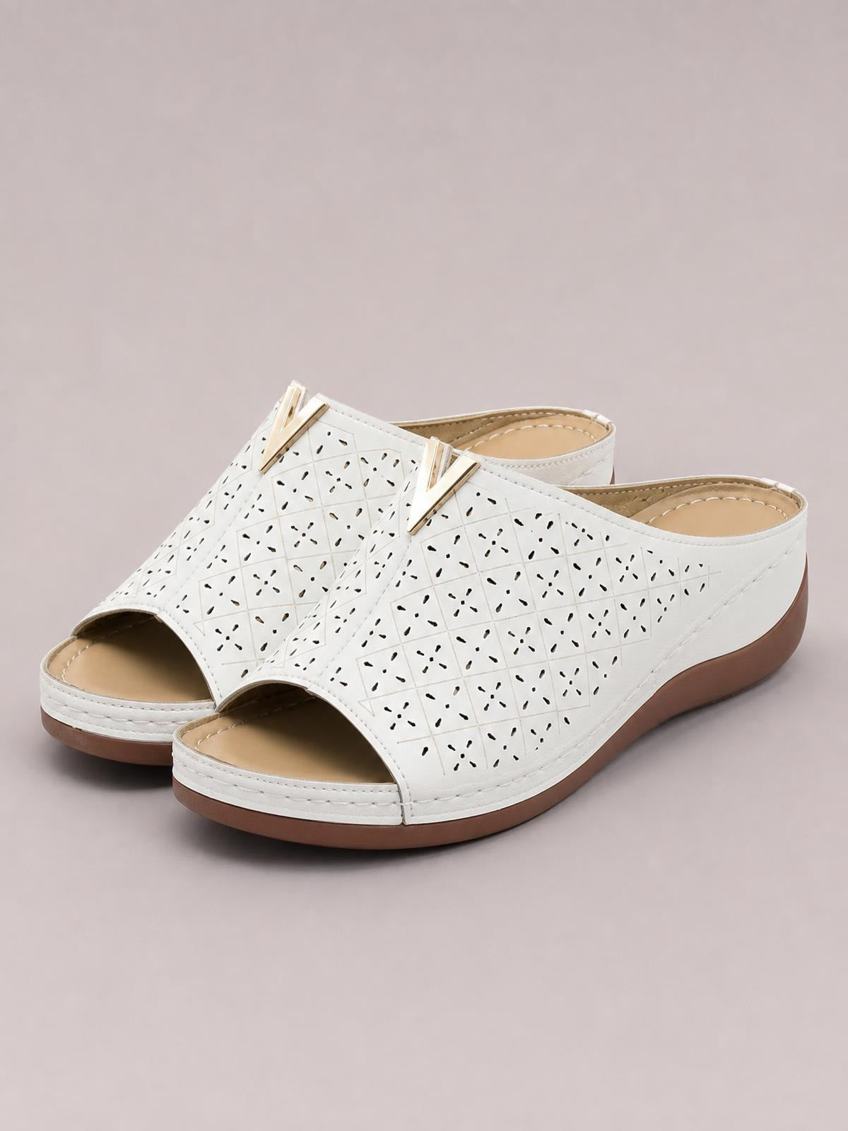 White open toe flat sandals with perforated geometric uppers, gold-tone accents, cushioned insoles, and contrasting brown rubber soles.