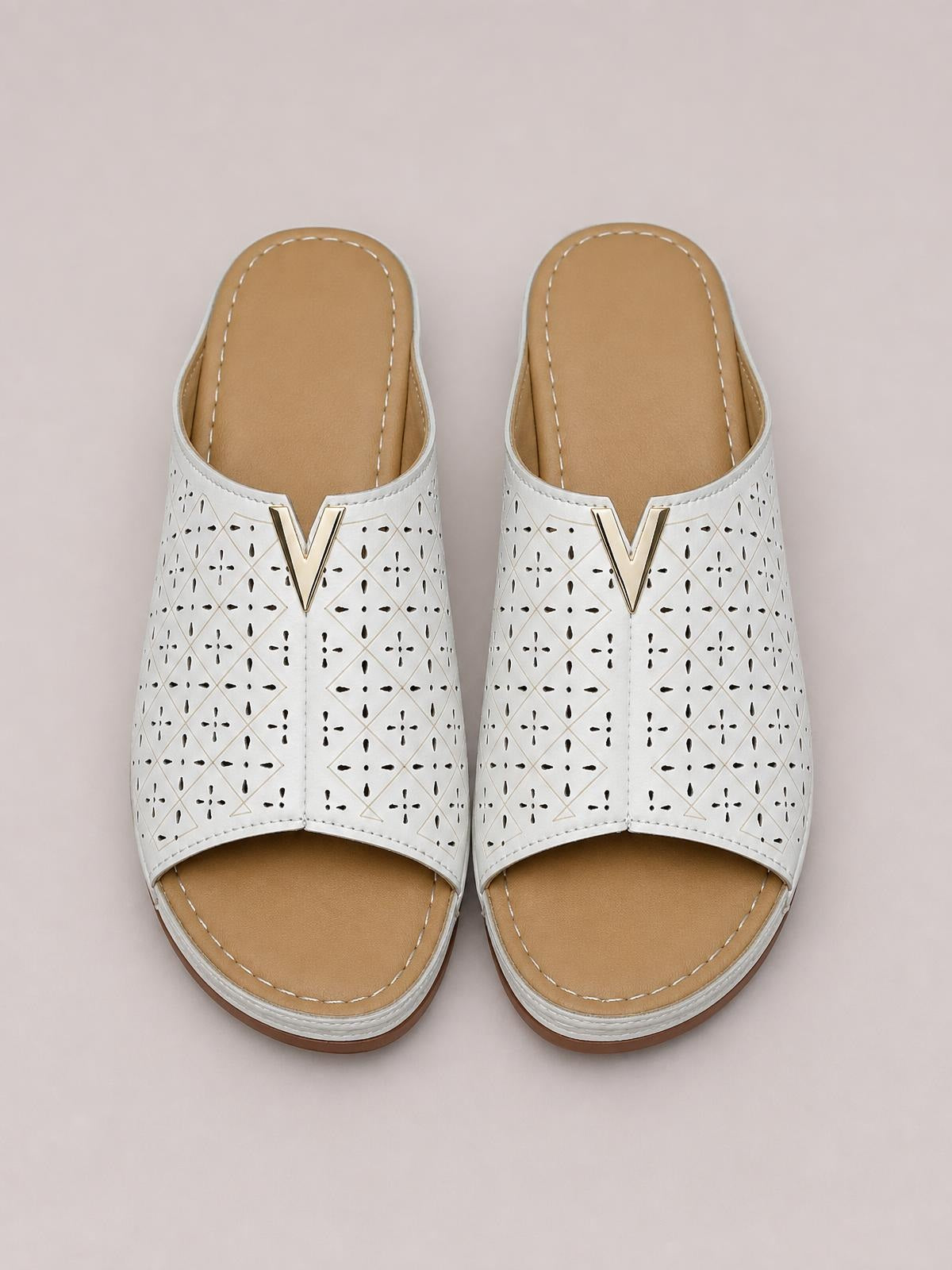 White open-toe flat sandals feature perforated geometric PU leather uppers, gold V-shaped accents, tan stitched footbeds, and low rubber soles.