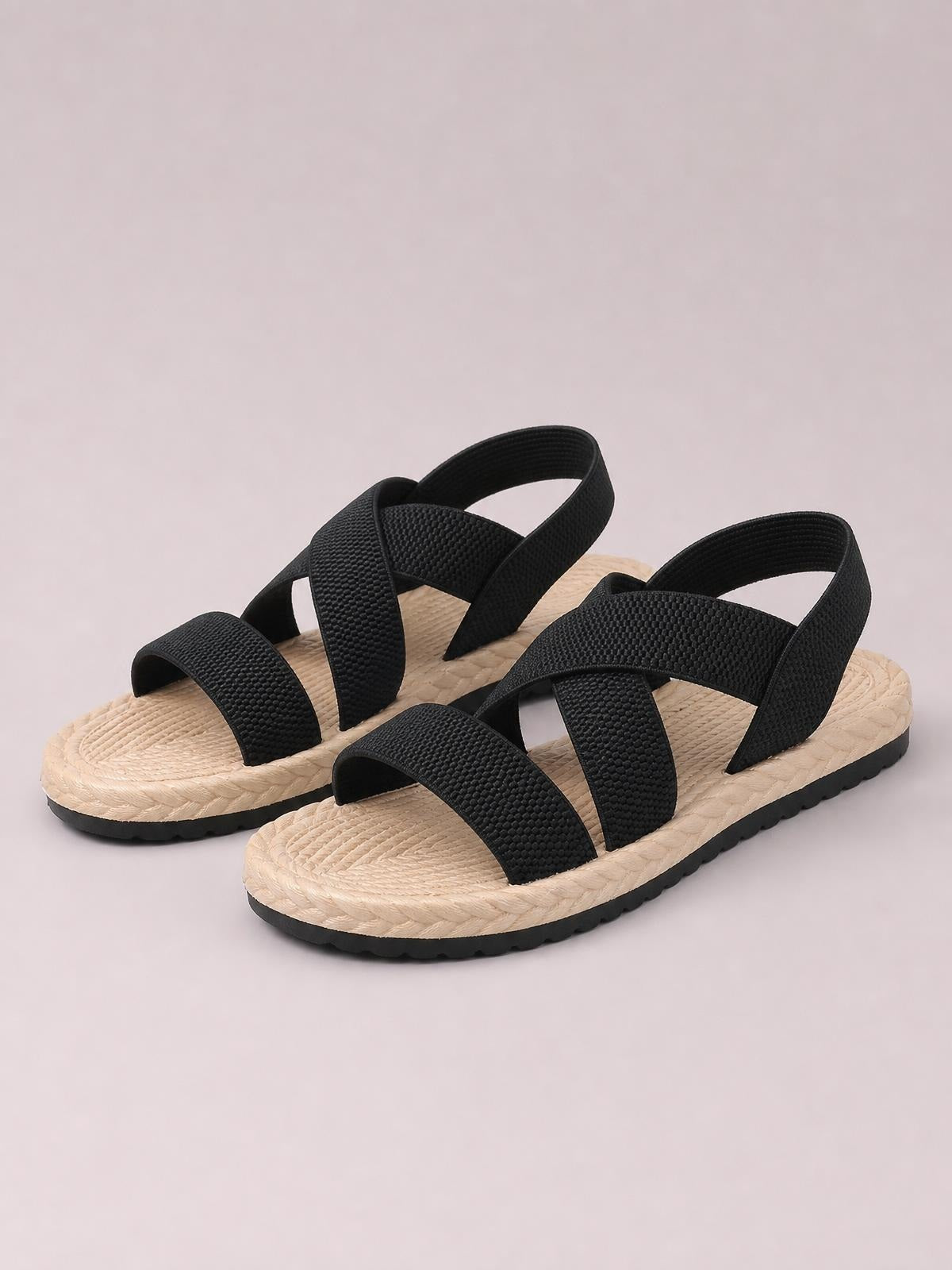Black open-toe flat sandals with wide crisscross straps, textured woven beige footbeds, adjustable heel bands, and contrasting black rubber soles.