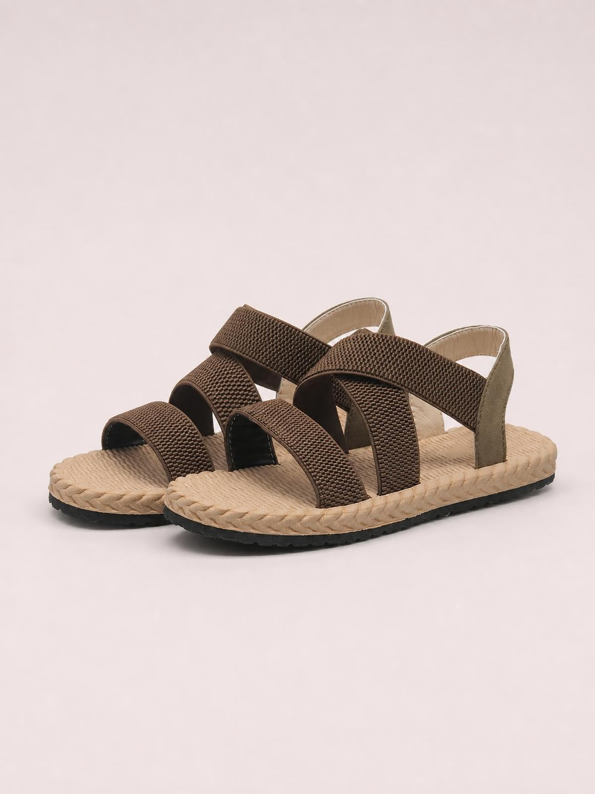 Brown open toe flat sandals feature textured woven cross straps, adjustable ankle straps, cushioned beige footbeds, and durable rubber soles.