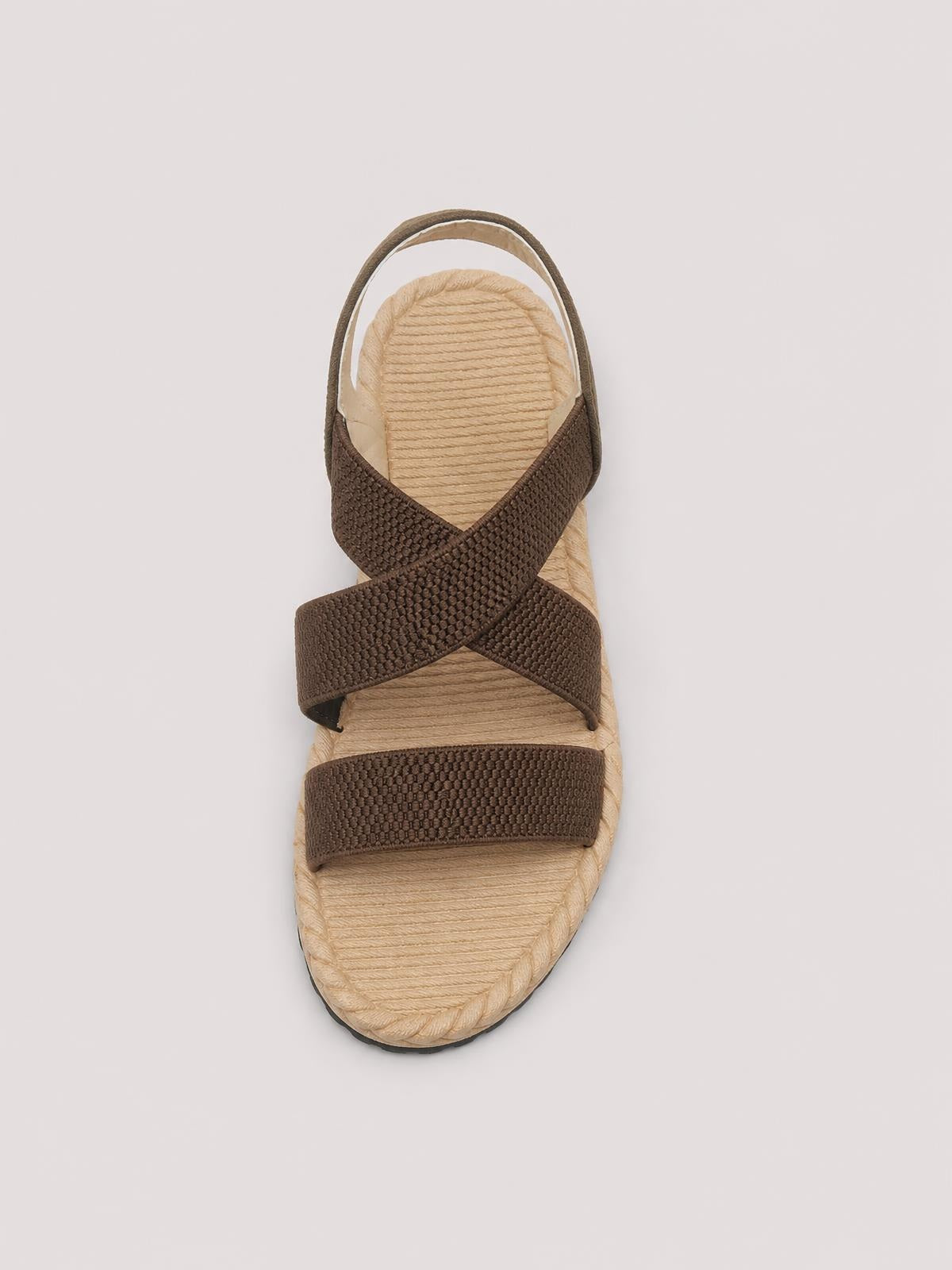 Brown open-toe flat sandal with textured woven straps crossing over a beige braided footbed, rounded toe, and slim heel strap.