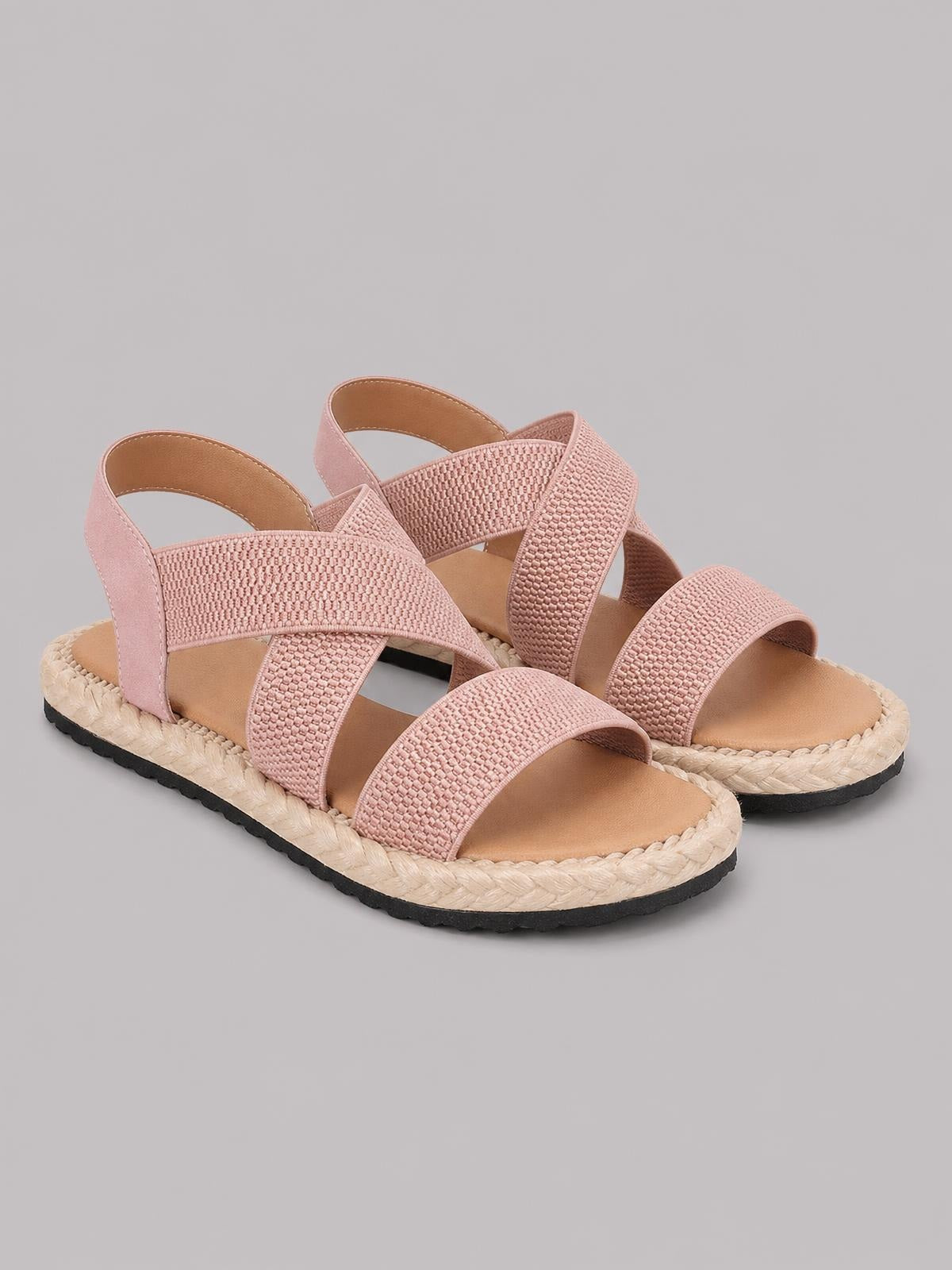 Pink open toe flat sandals with textured crisscross straps, ankle straps, cushioned footbeds, braided platform-style trim, and black rubber soles.