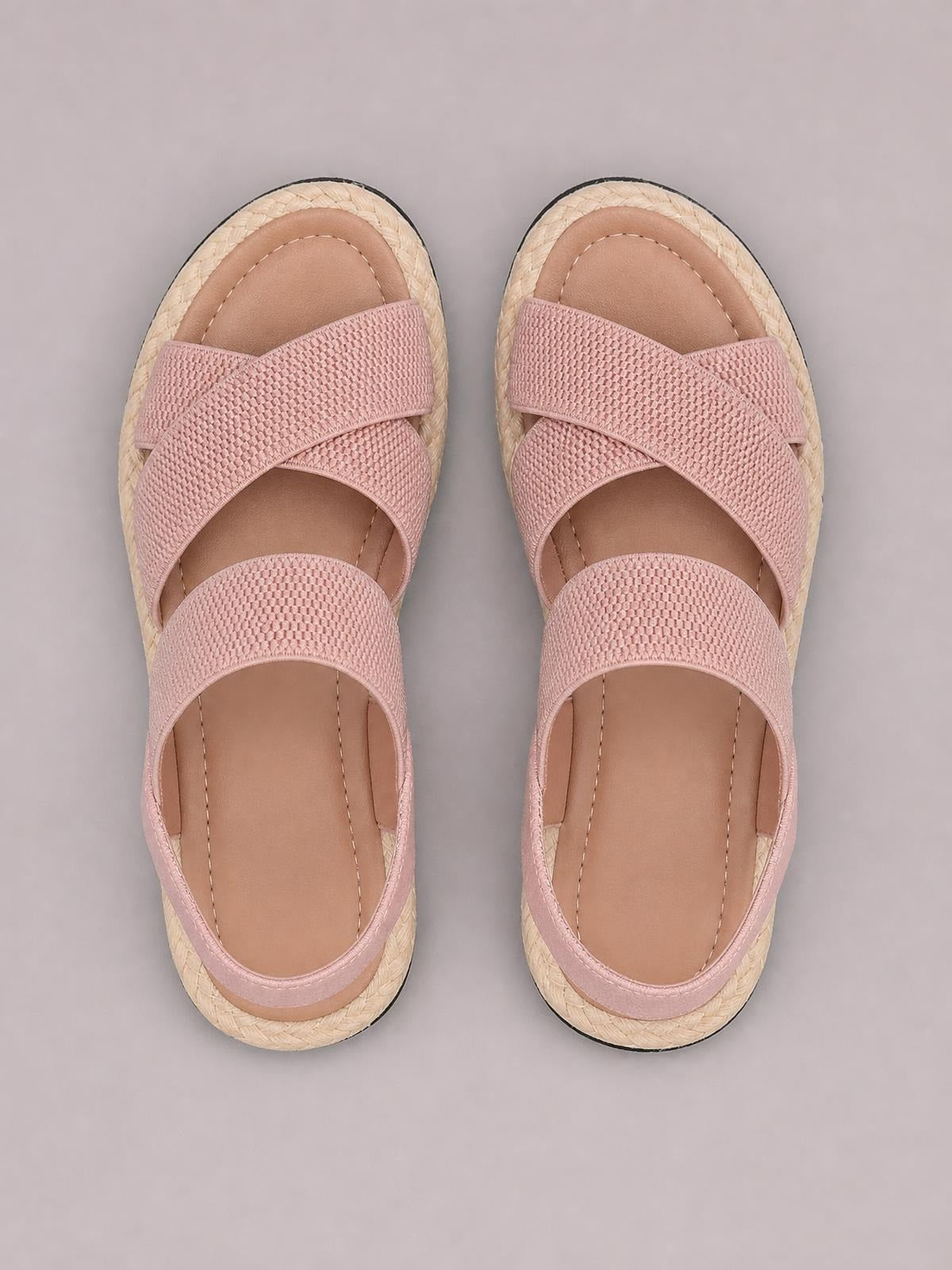 Pink open toe flat sandals with textured crisscross straps, cushioned footbeds, and woven espadrille-style soles.