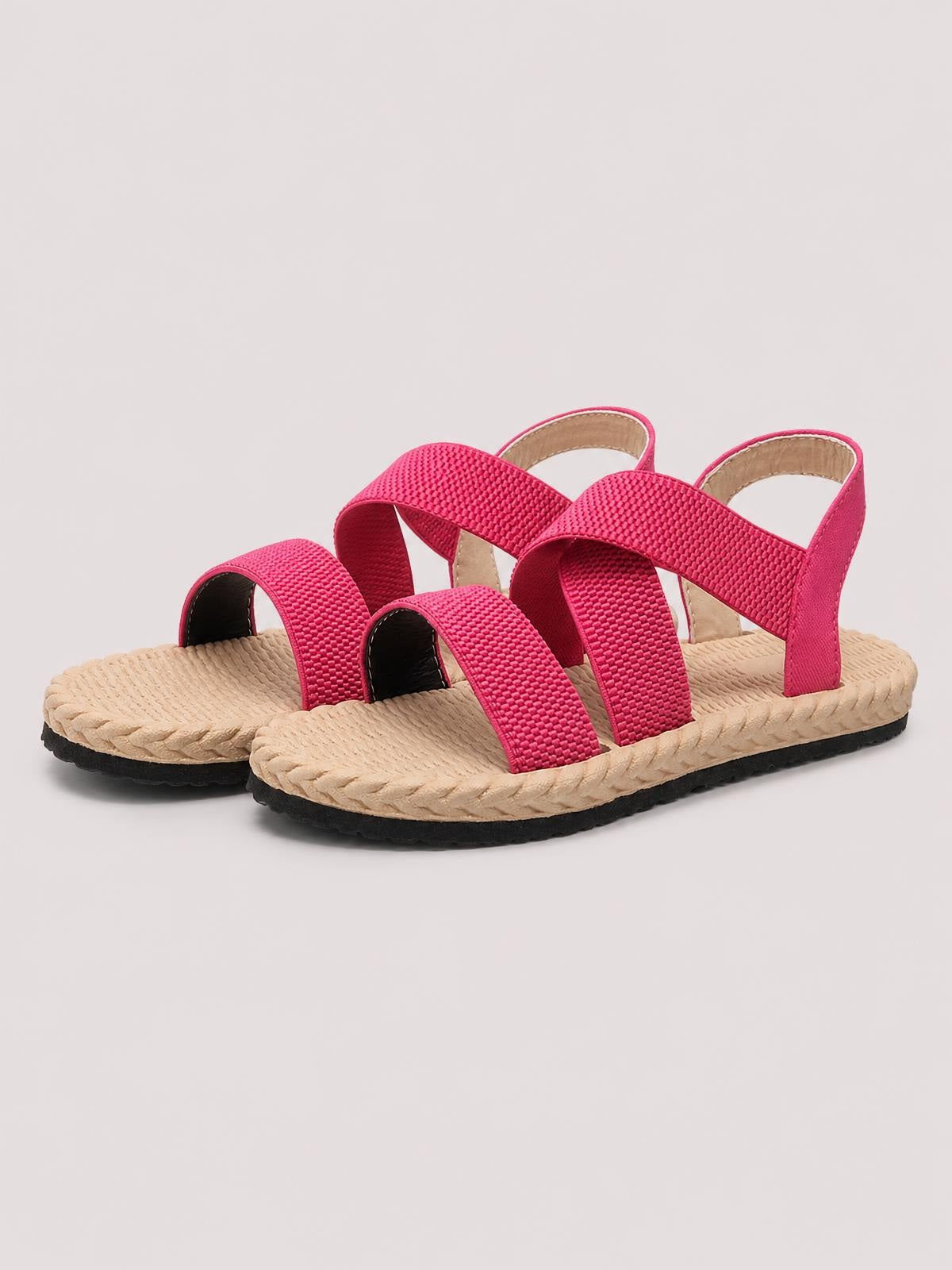 Bright pink open-toe flat sandals feature wide woven straps, slingback ankle bands, textured beige footbeds, braided edges, and black rubber soles.