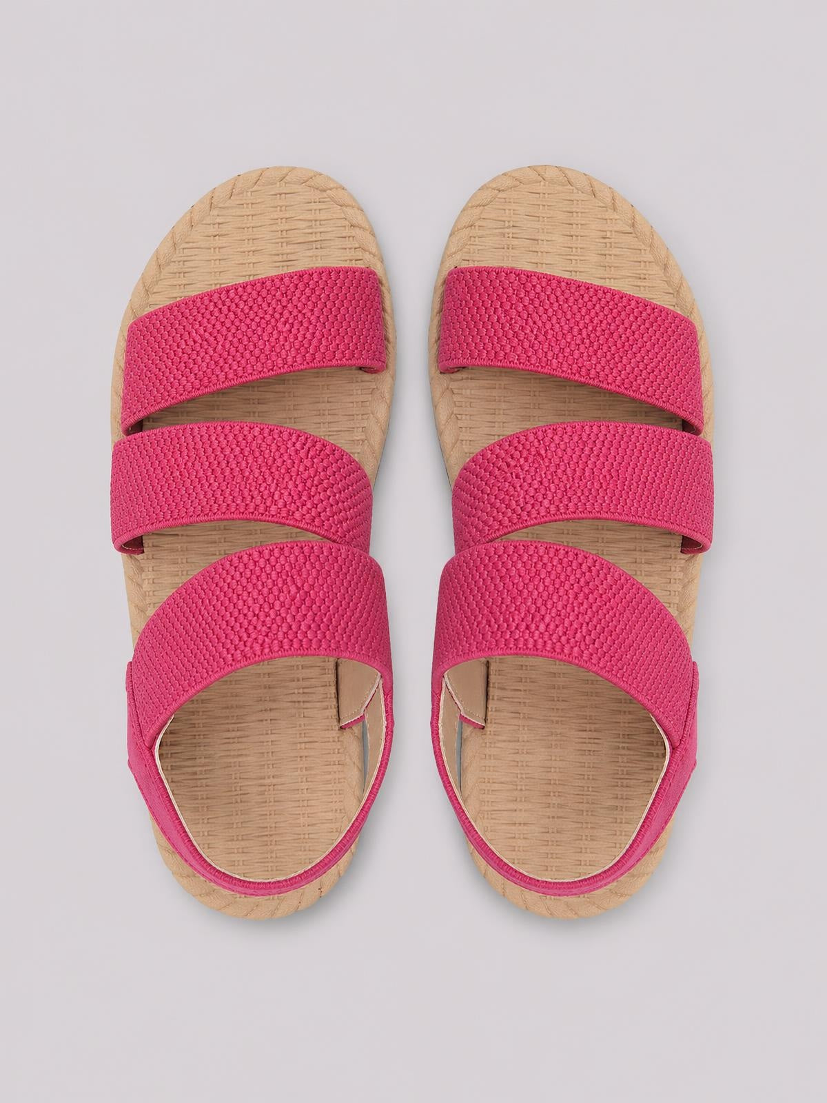 Bright pink open toe flat sandals feature three wide textured straps, rounded toes, and natural beige woven footbeds with matching flat soles.