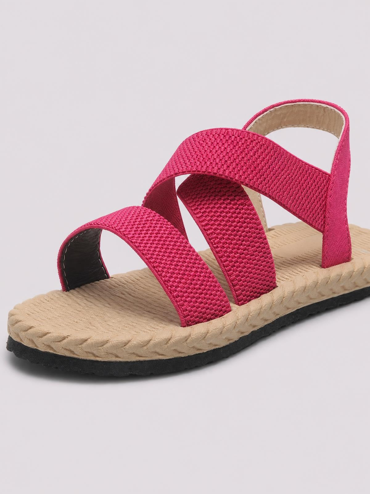 Pink open-toe flat sandals feature multiple woven straps, a beige textured footbed, a supportive back strap, and a black rubber sole.