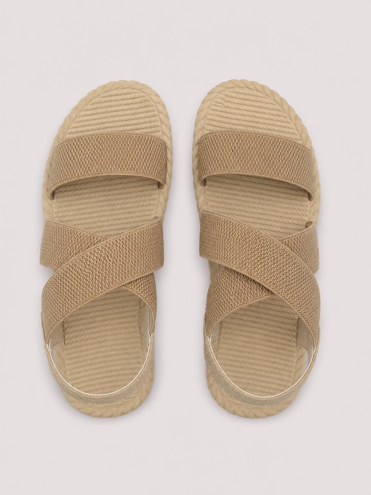 Beige open toe flat sandals with wide textured straps crossing over the foot, ribbed footbeds, and flexible-looking rubber soles.