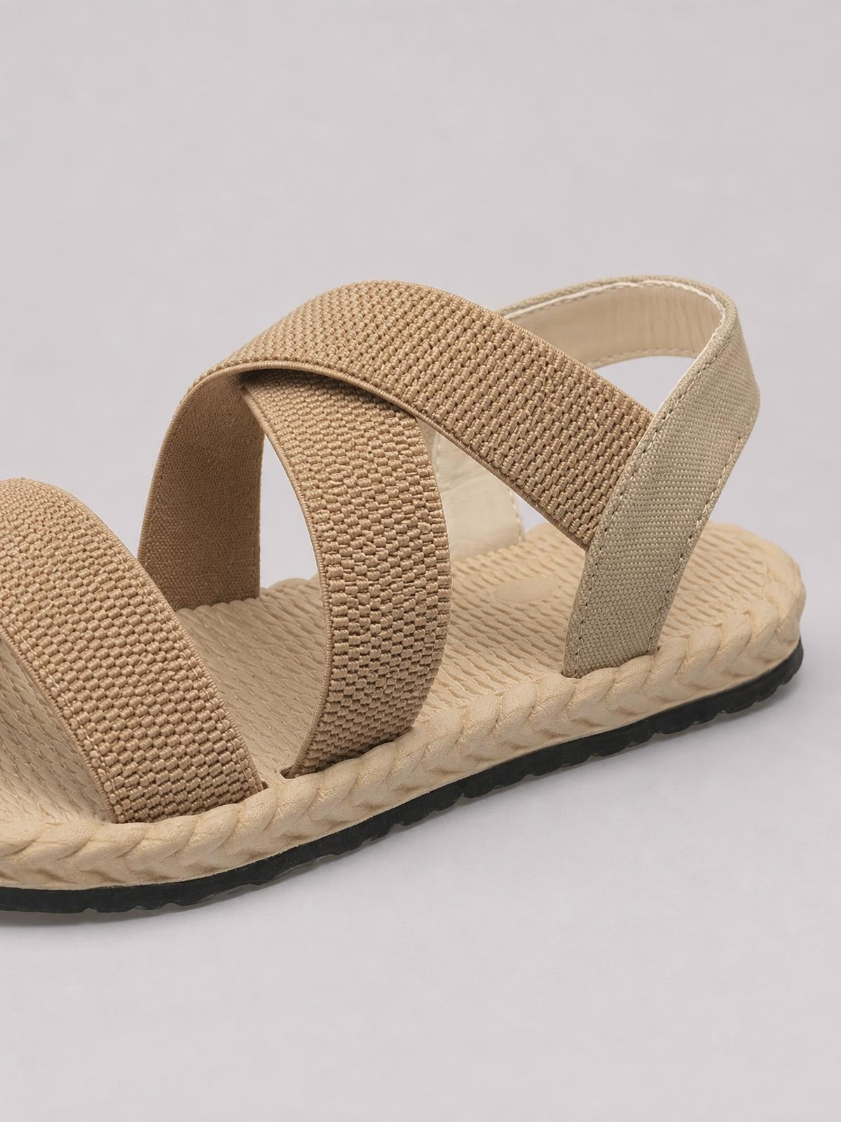 Tan open-toe flat sandals feature multiple wide woven straps, a textured footbed, braided trim, and a durable black rubber sole.