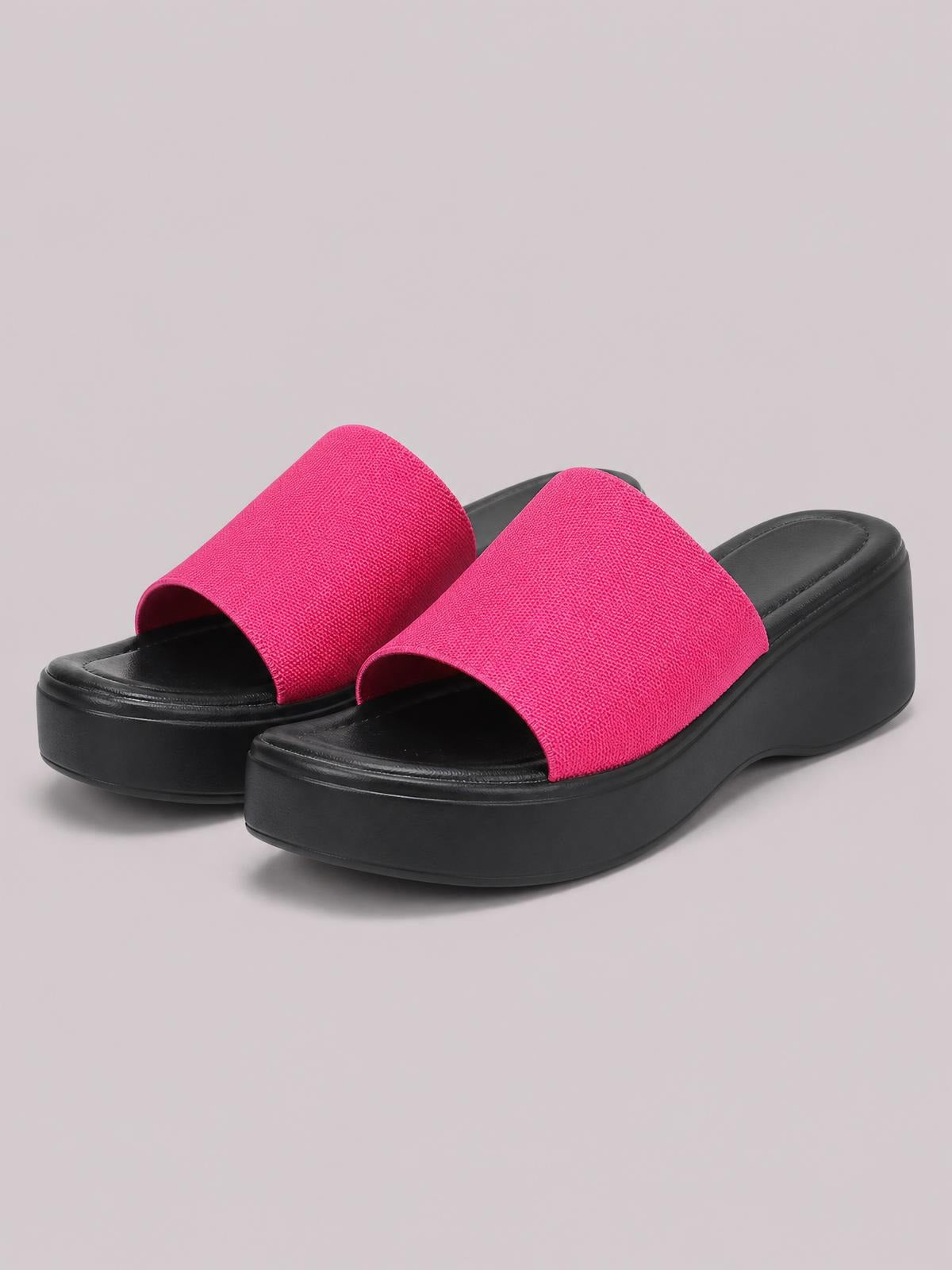 Bright pink open toe platform cloth sandals feature wide single straps, black cushioned footbeds, and thick black rubber wedge soles.