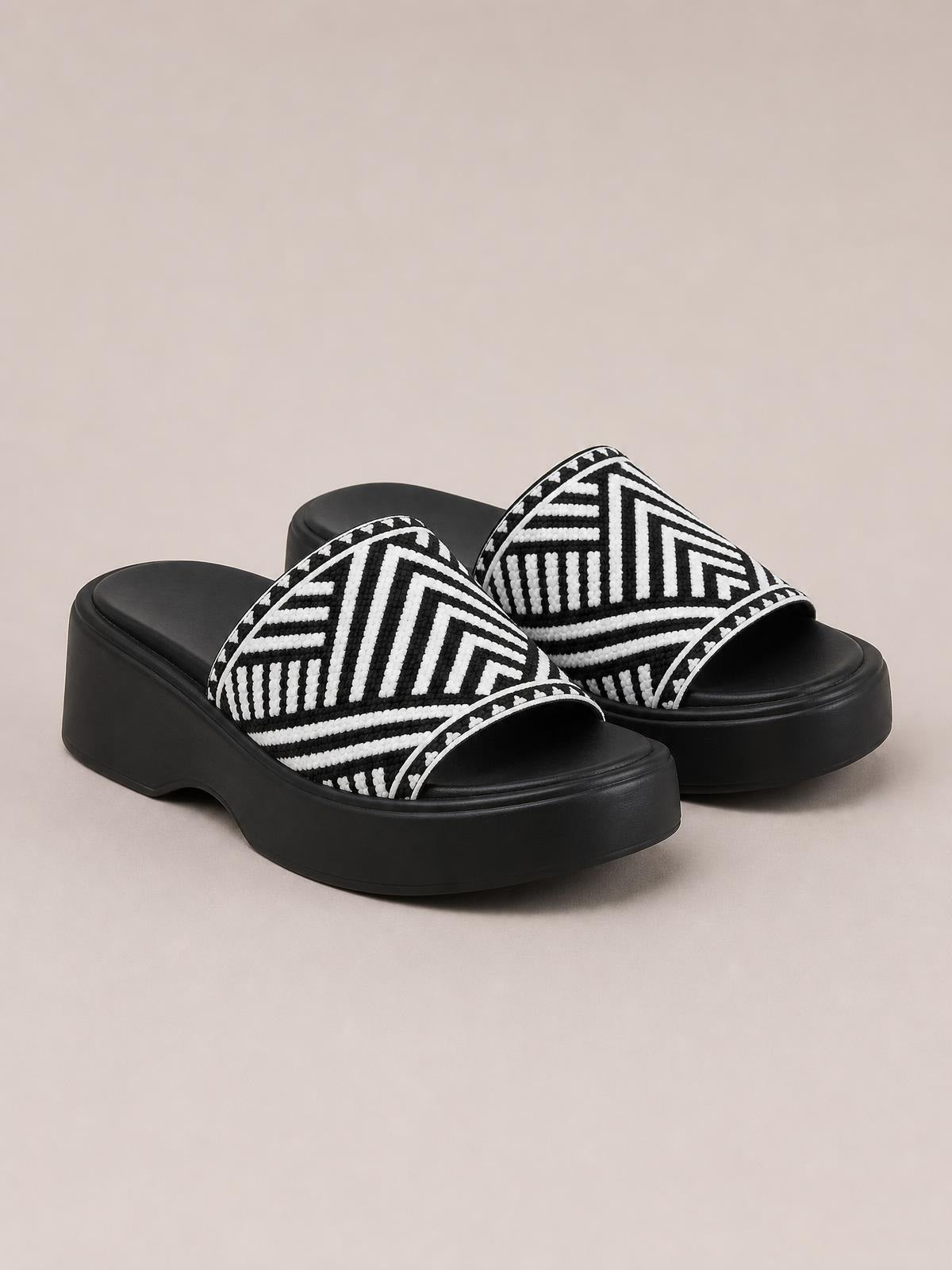 Black and white open-toe cloth sandals feature bold geometric-patterned straps and thick black rubber platform soles.