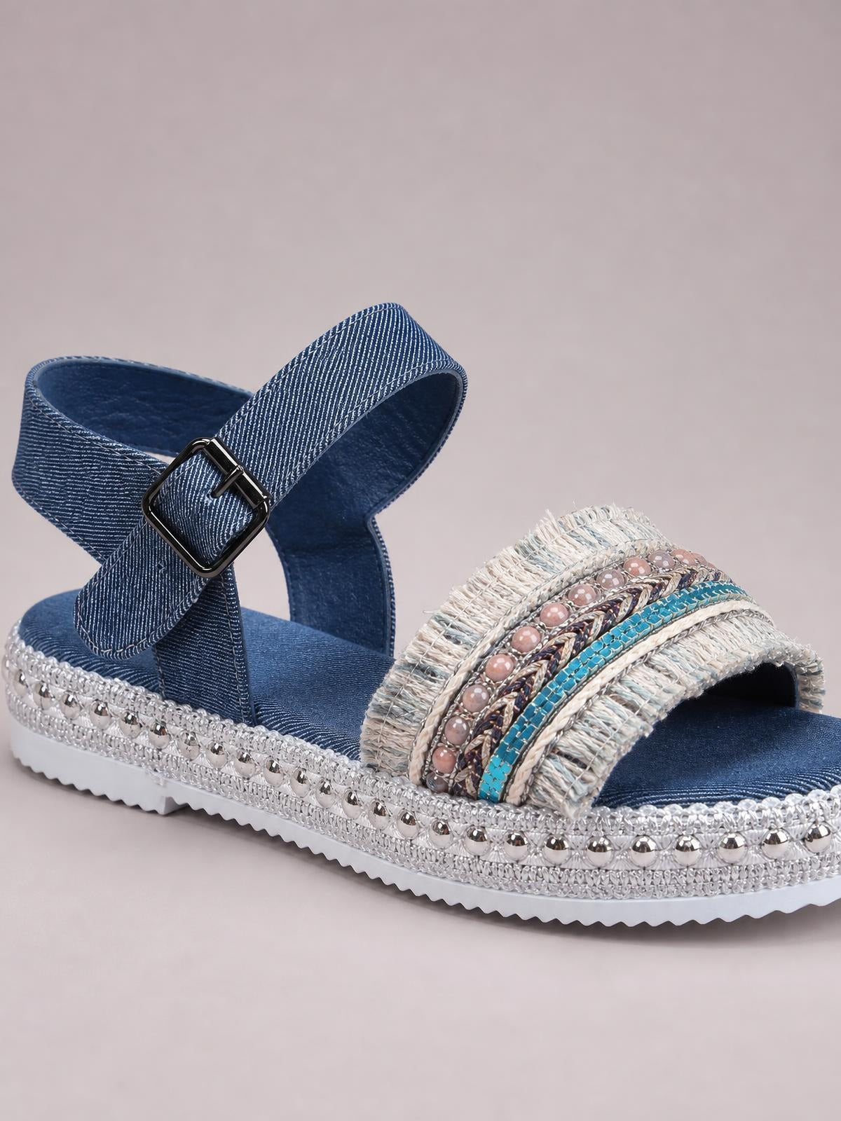 Blue denim open toe platform sandals feature an adjustable ankle buckle, embellished crisscross straps, studded trim, and a white rubber sole.