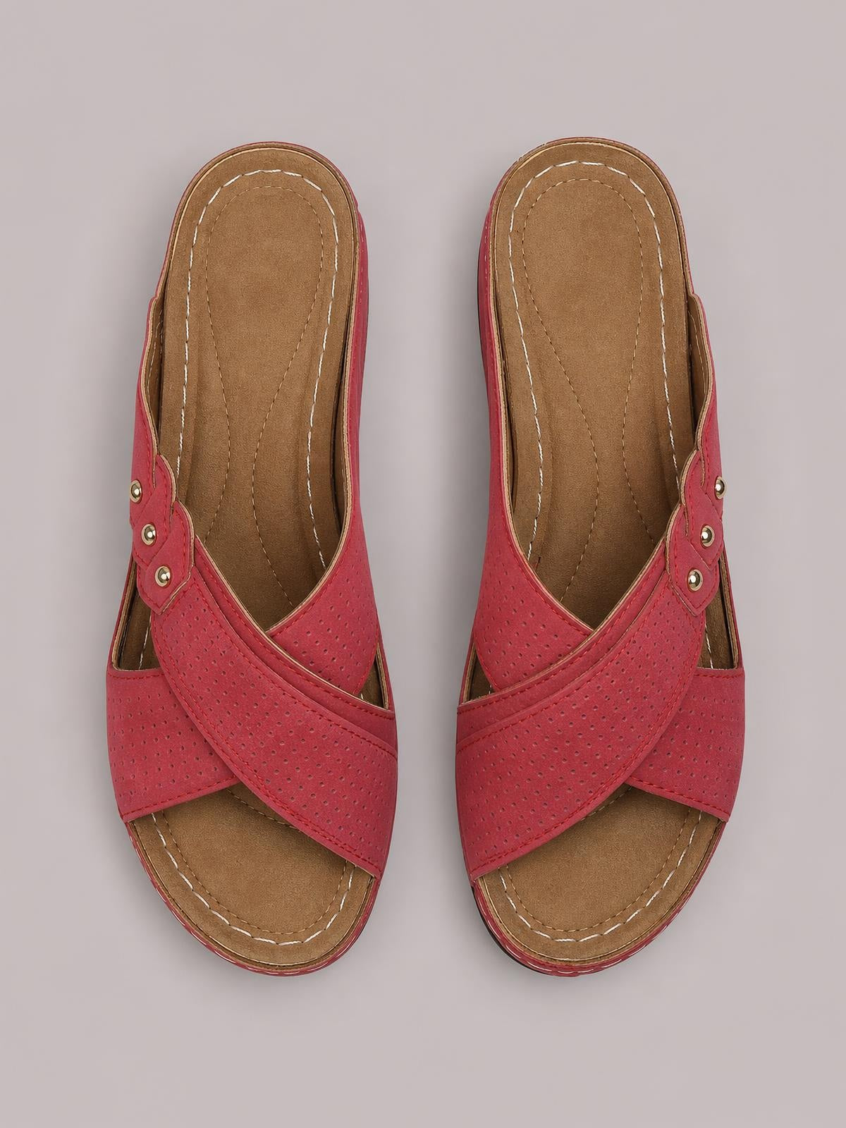 Red open-toe platform sandals with crossed perforated straps, stitched cushioned footbeds, and decorative side studs in a flat silhouette.