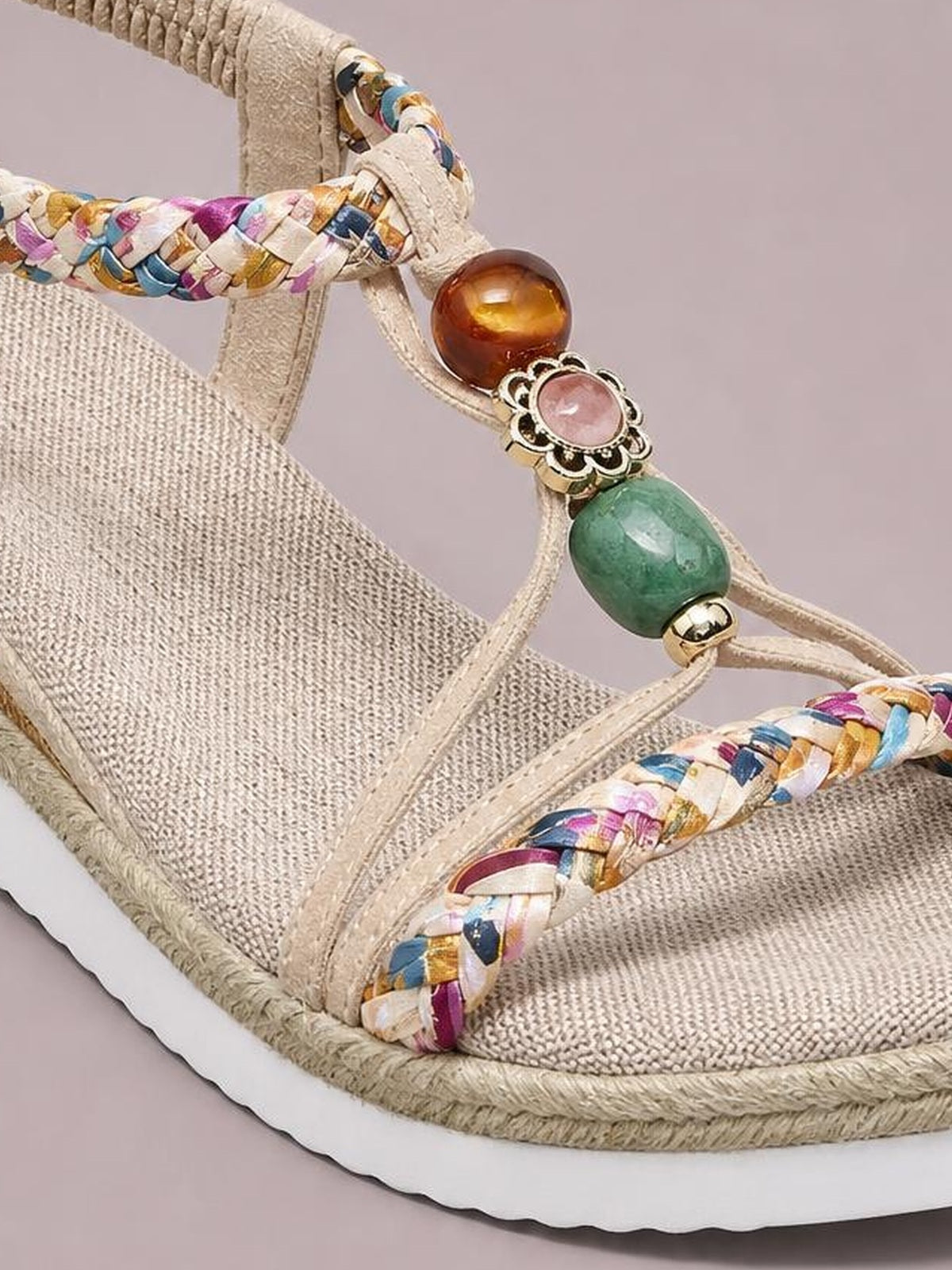 Close-up of open-toe platform wedge sandals with beige woven footbeds, colorful braided straps, decorative beads, and thick white midsoles.