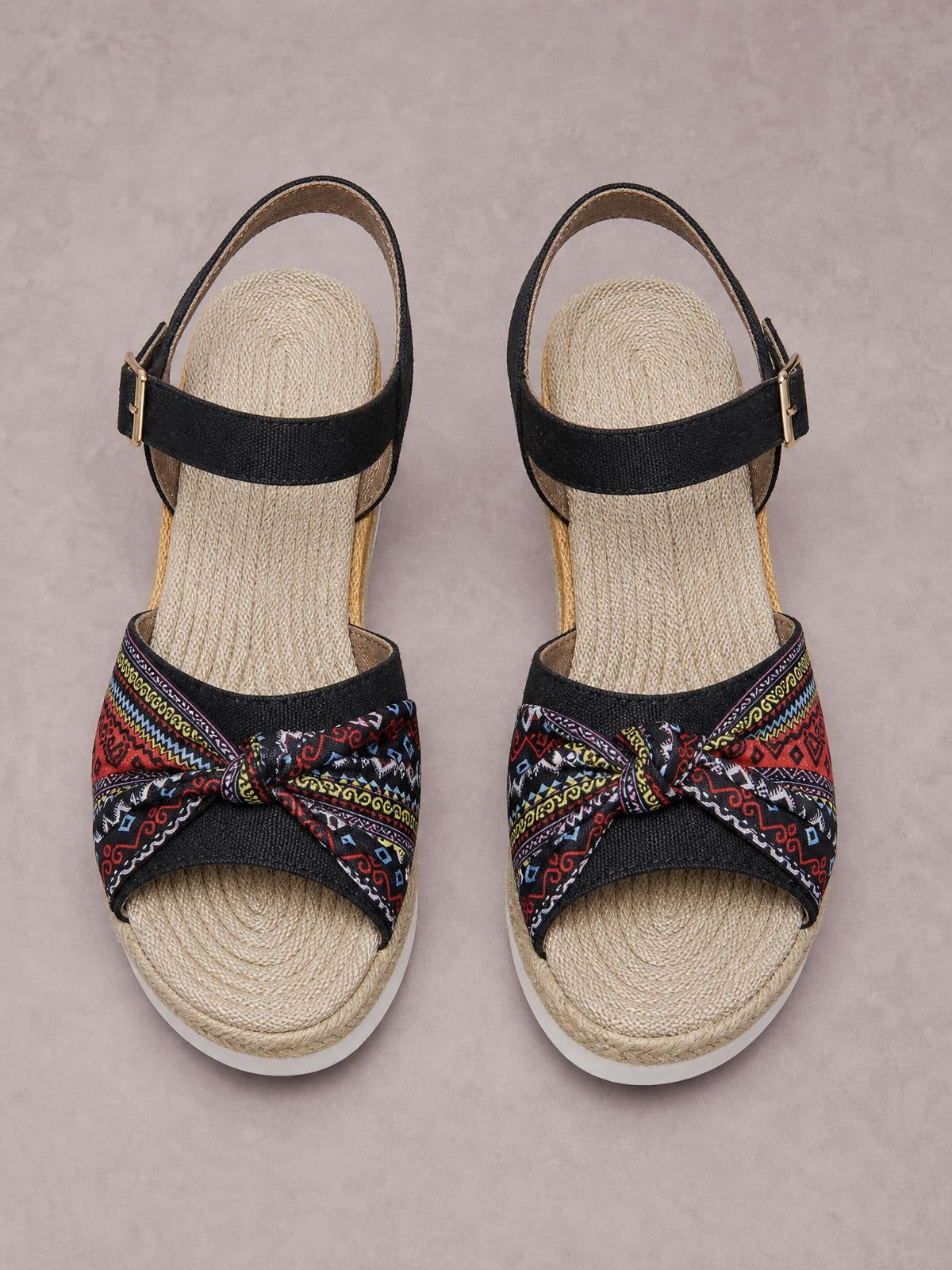 Black open-toe platform wedge sandals feature colorful patterned bow straps, ankle buckle closures, woven espadrille-style soles, and comfortable mid-height heels.