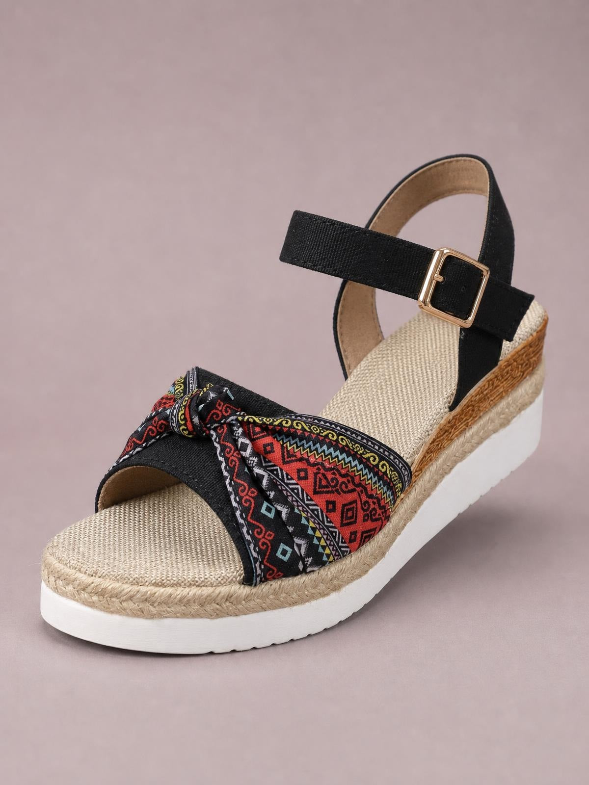 Black open toe platform wedge sandal with a colorful patterned bow strap, adjustable gold-tone ankle buckle, woven espadrille trim, and white mid-height platform sole.