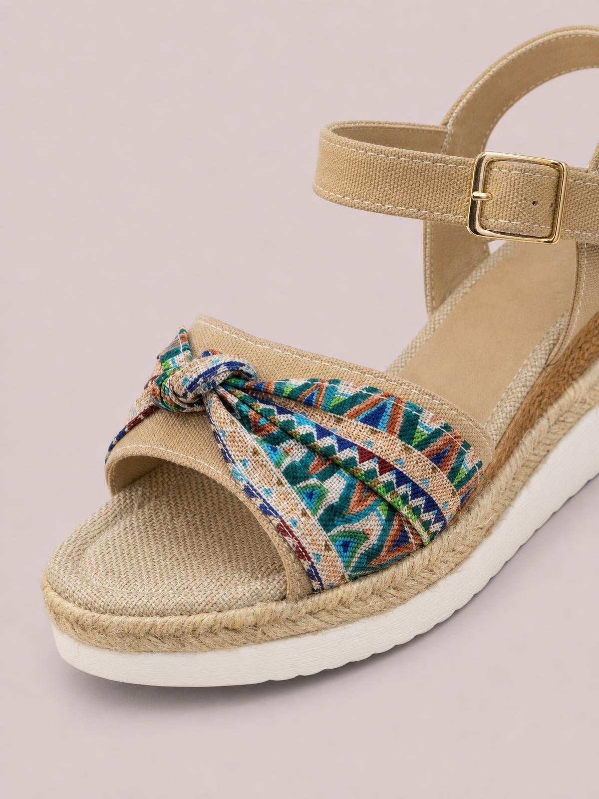 Tan open toe platform wedge sandal with a colorful patterned bow, woven espadrille-style trim, ankle strap, gold buckle, and mid-height heel.