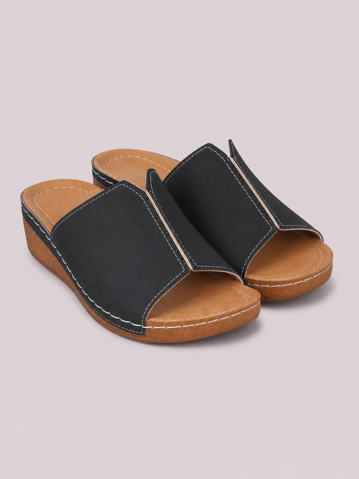 Black open-toe wedge sandals with wide stitched upper straps, tan cushioned footbeds, and low textured wedge soles.