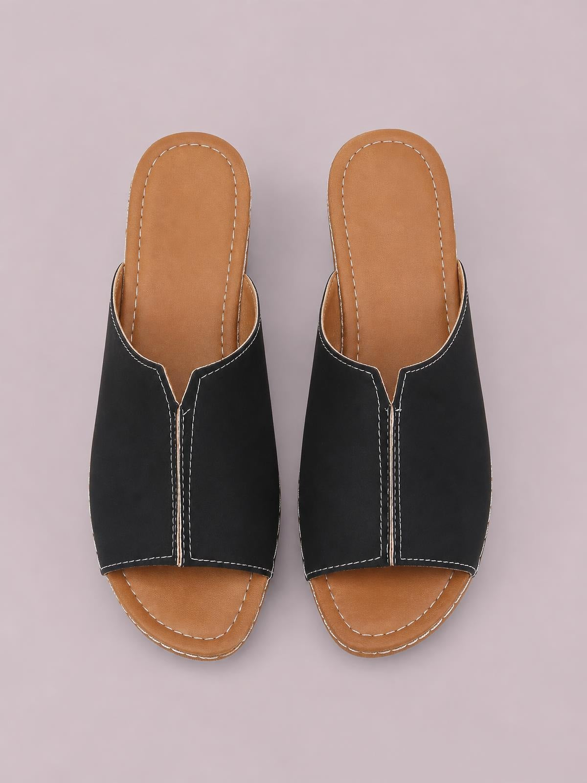 Black open-toe wedge sandals feature wide slip-on uppers, tan contoured footbeds, contrasting white stitching, and low stacked wedge soles.