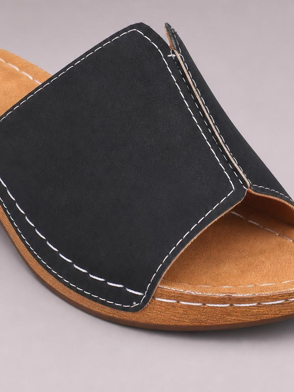 Black open-toe wedge sandal with a broad upper strap, contrasting white stitching, and a tan textured footbed on a low platform sole.