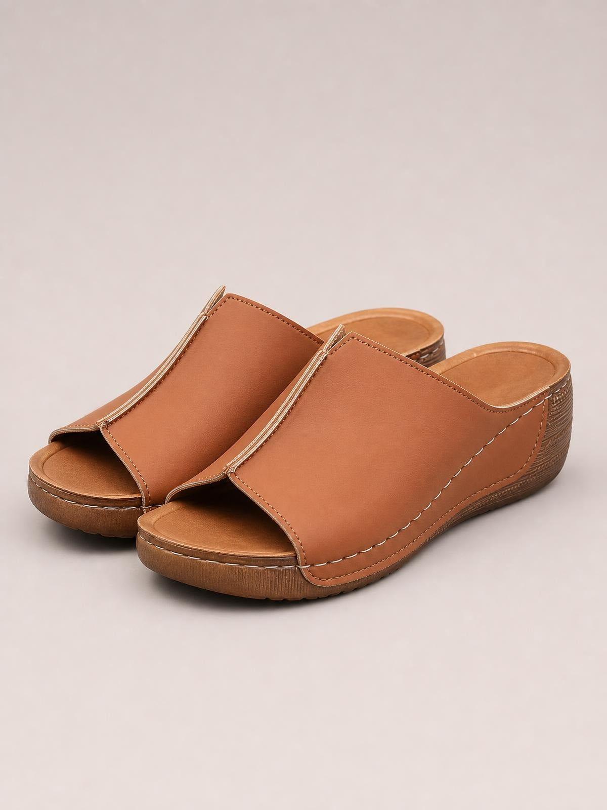 Brown open toe wedge sandals feature wide stitched uppers, cushioned footbeds, and low textured wedge heels with a comfortable slip-on silhouette.