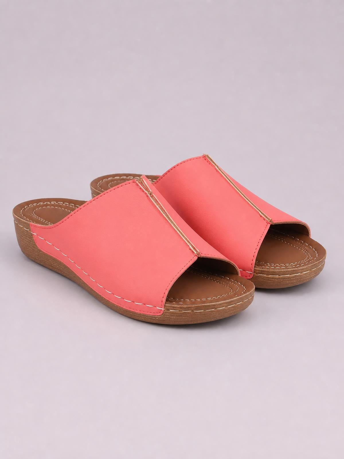 Coral pink open toe wedge sandals feature wide slip-on uppers with gold-tone trim, stitched details, cushioned footbeds, and low brown wedge soles.