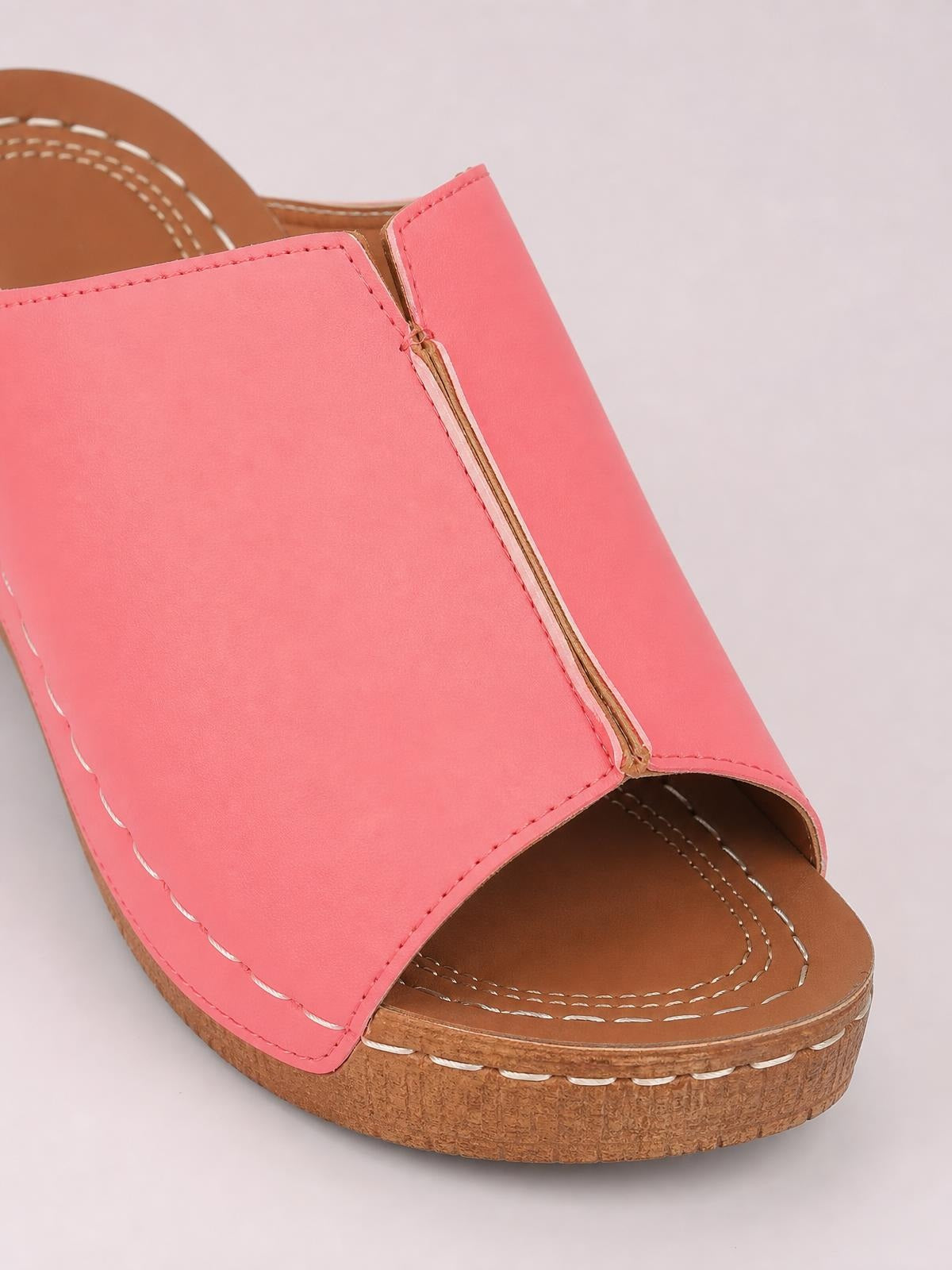 Close-up of a coral pink open-toe wedge sandal with a wide stitched upper, brown footbed, and low cork-textured wedge sole.
