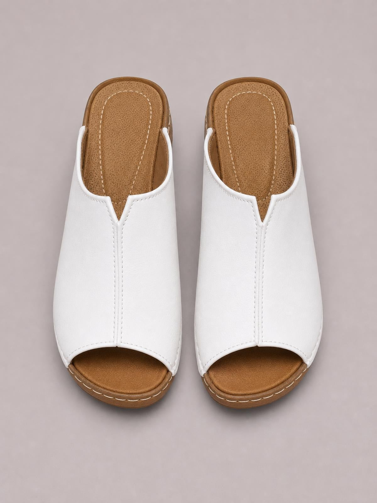 White open-toe wedge sandals feature broad stitched uppers, brown contoured footbeds, and low textured wedge soles.