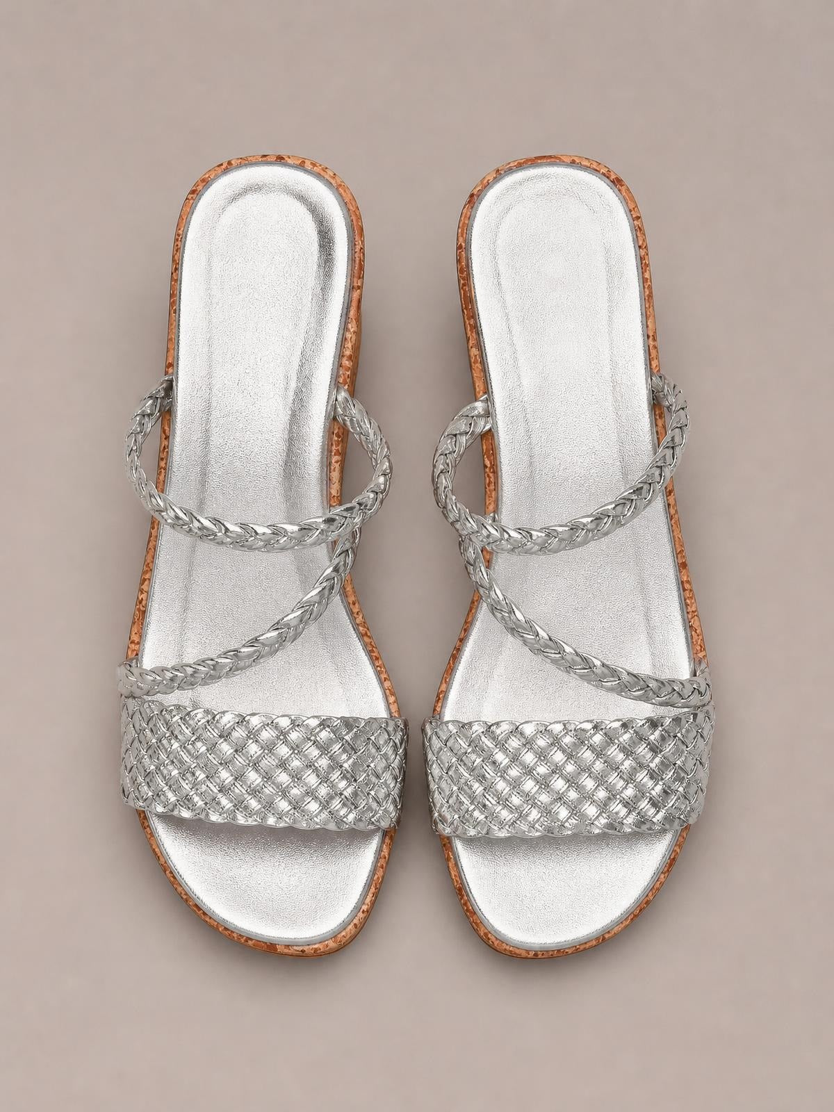 Silver open toe wedge sandals with woven wide front straps, braided crossover straps, metallic footbeds, and warm brown-trimmed soles.