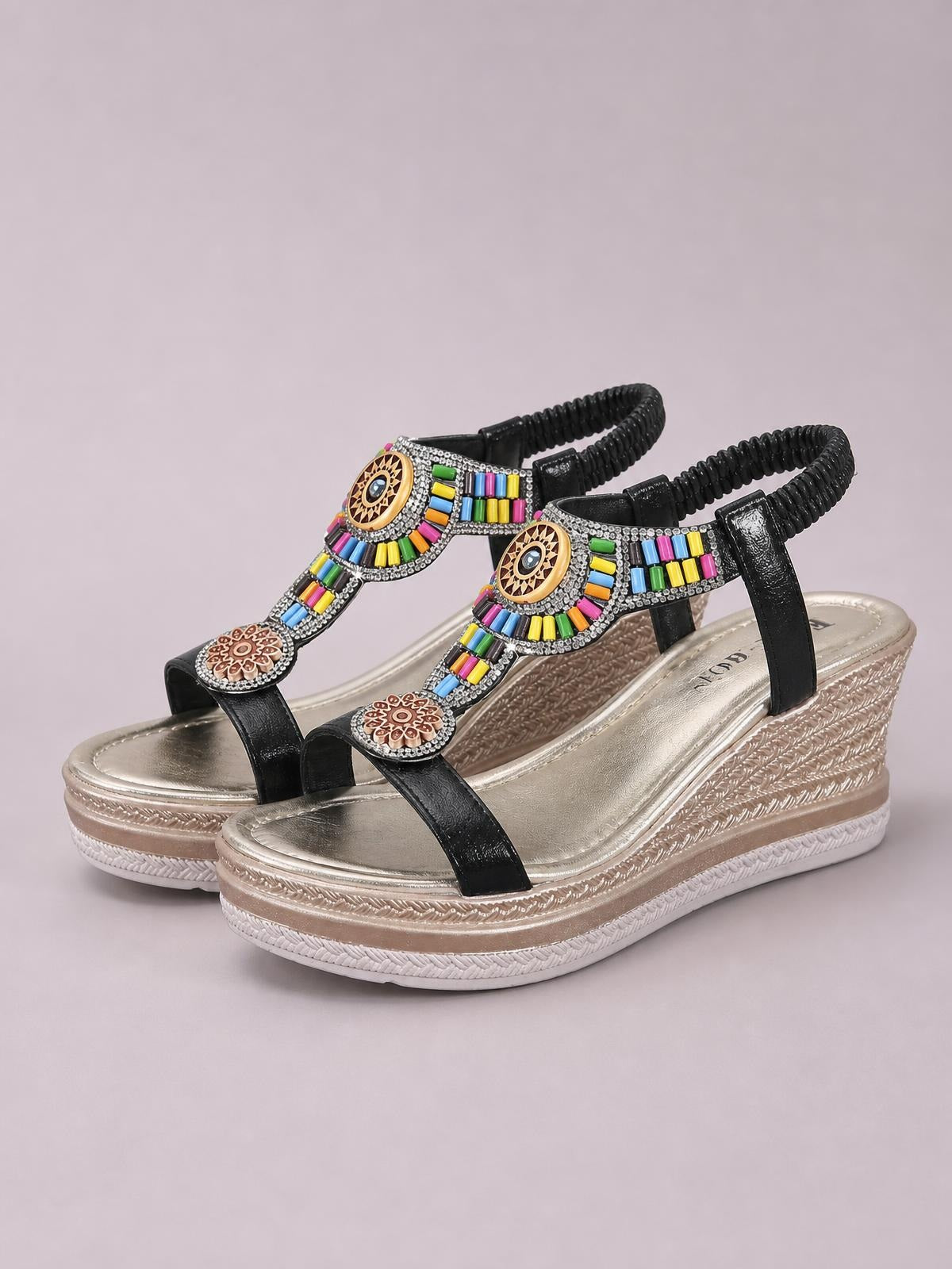 Open toe wedge sandals feature black straps, colorful beaded embellishments, decorative medallions, and a metallic gold mid-height platform wedge sole.