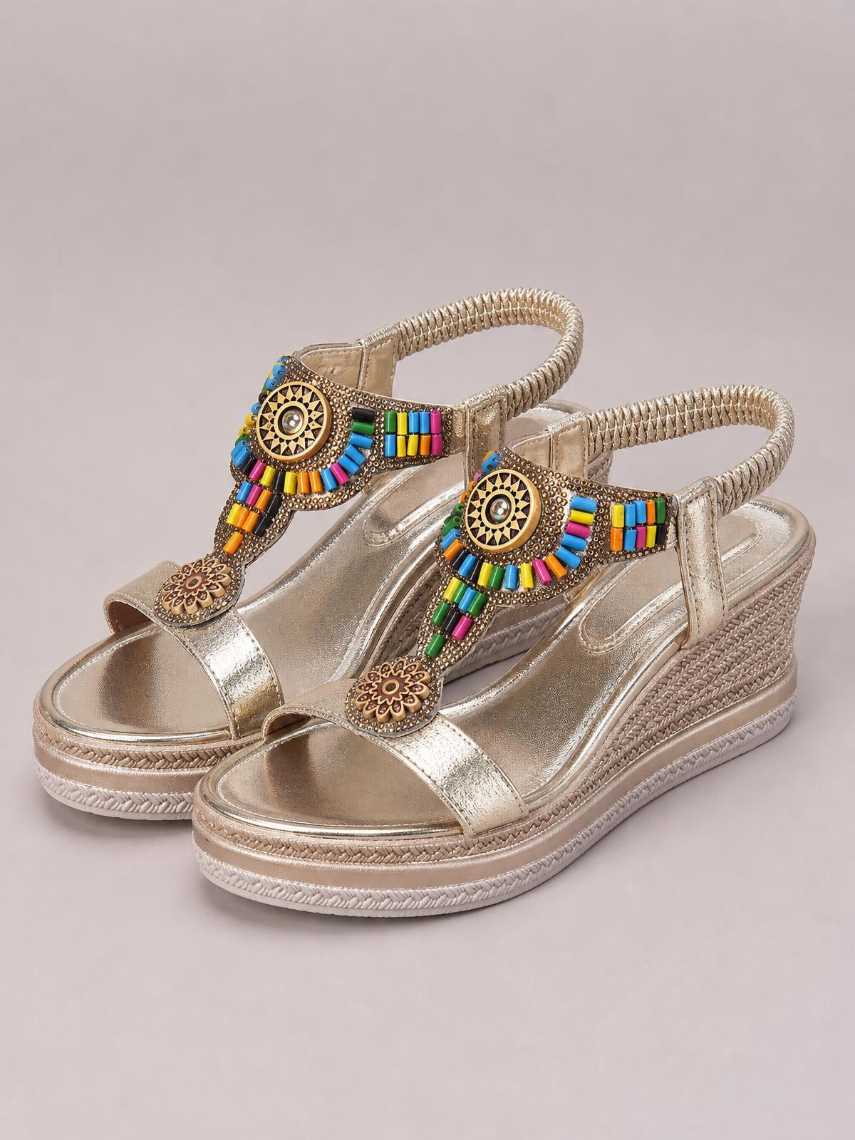 Metallic gold open toe wedge sandals feature braided ankle straps, colorful beaded embellishments, decorative medallions, and textured mid-height platform soles.