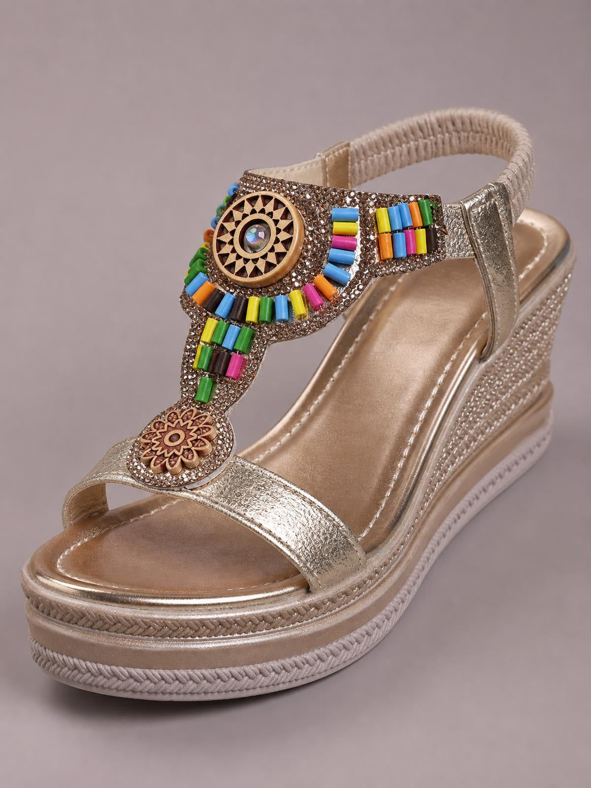 Metallic gold open toe wedge sandals feature a mid-height platform sole, jeweled multicolor beaded straps, an ankle strap, and braided trim.