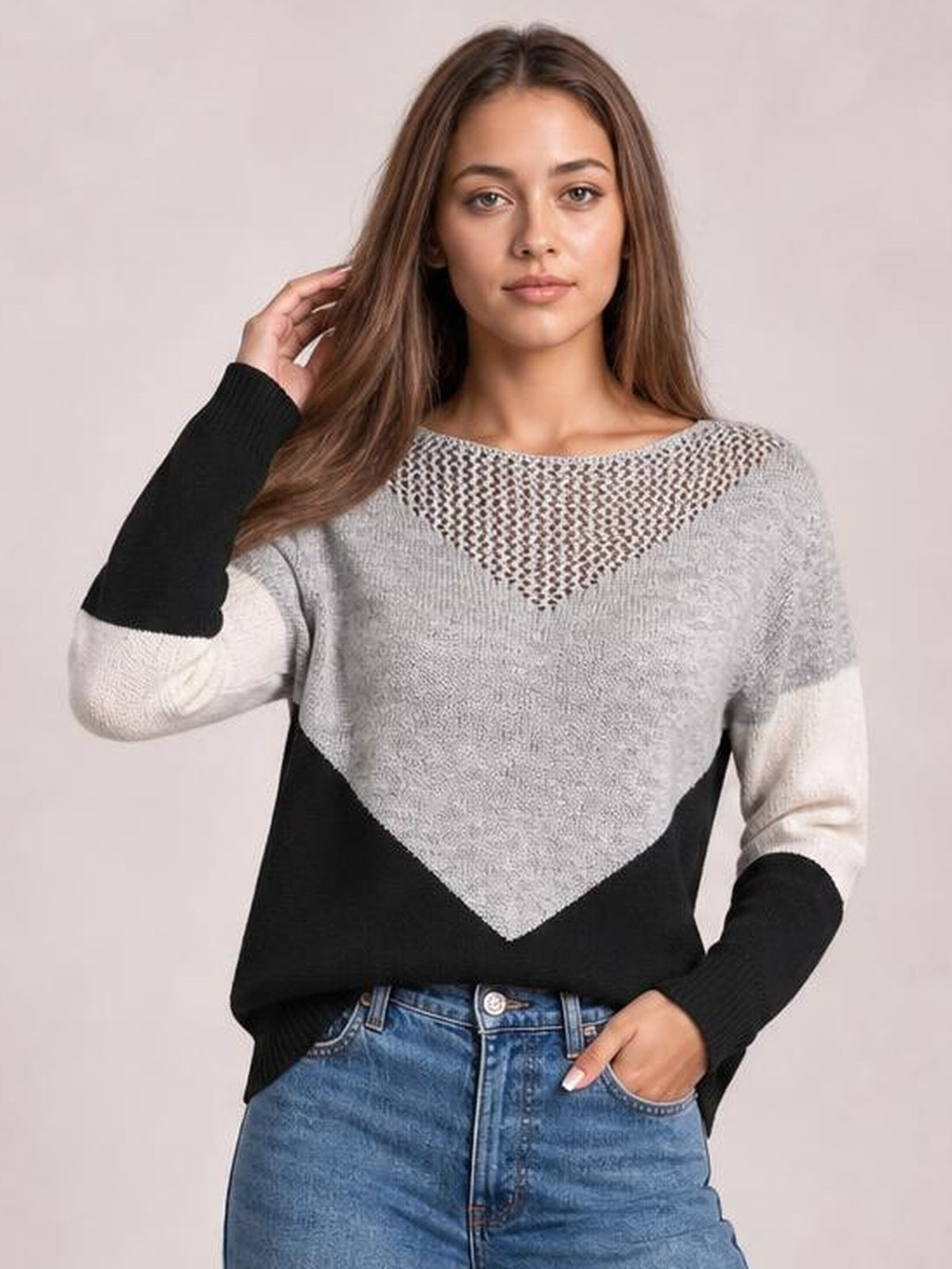 Model poses in a color-block long-sleeve sweater with gray, black, and cream panels, a relaxed silhouette, and an openwork V-shaped chest detail.