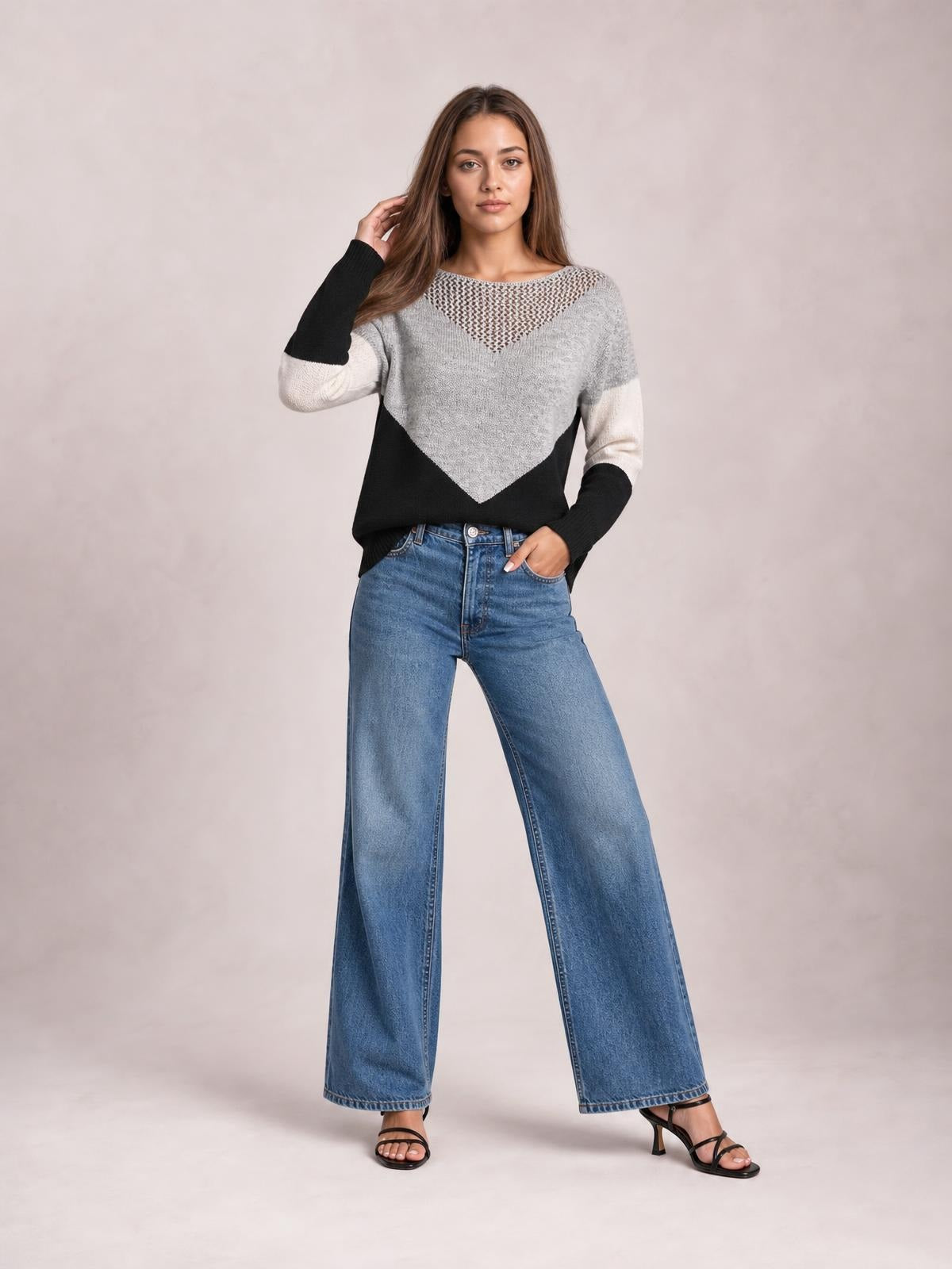 Model poses in a relaxed color-block sweater with long sleeves, gray, black, and cream panels, a V-shaped openwork yoke, and a loose straight silhouette.
