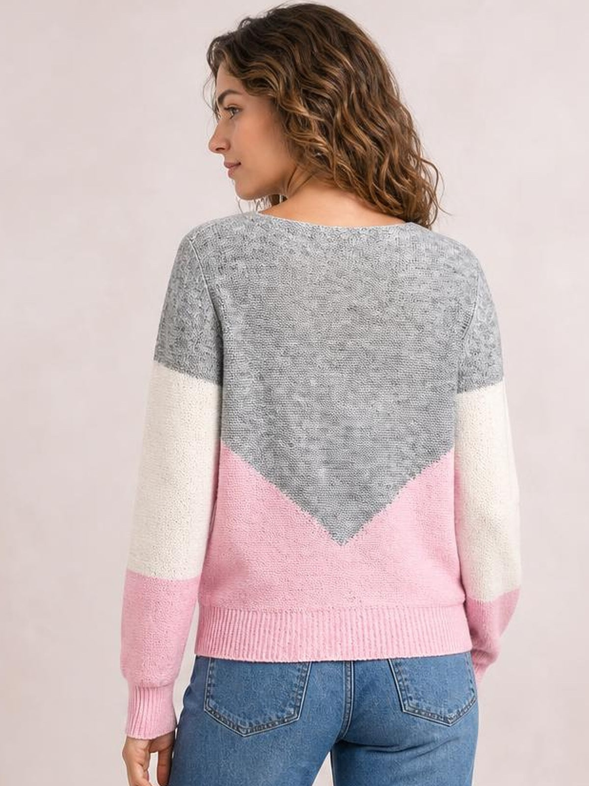 Model turned away displays a relaxed-fit openwork color block sweater with long sleeves, gray and pink sections, cream sleeve bands, ribbed cuffs, and hem.