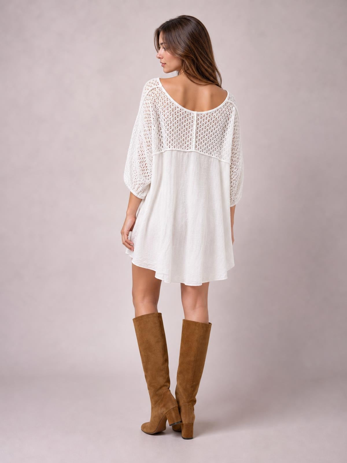 Model turned to show the back of a white oversized top with openwork sleeves and yoke, exposed seams, and a flowing high-low hem.