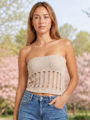 Model wearing a cream openwork knit tube top with a strapless neckline, fitted silhouette, and vertical cutout detailing, posing with one hand in her jeans pocket.
