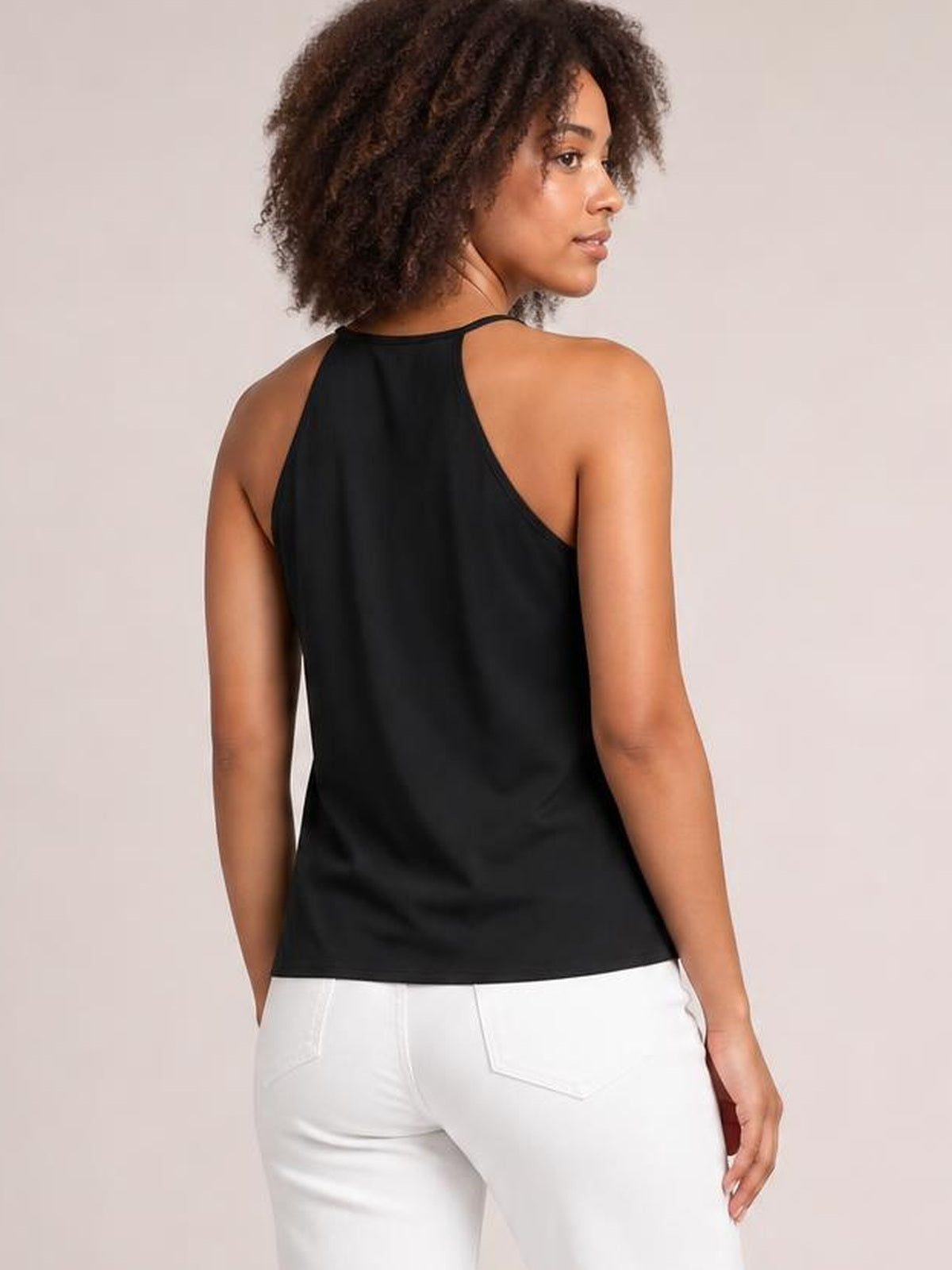 A model turned slightly wears a black cami with slim straps, a high back neckline, and a relaxed straight silhouette ending at the hips.