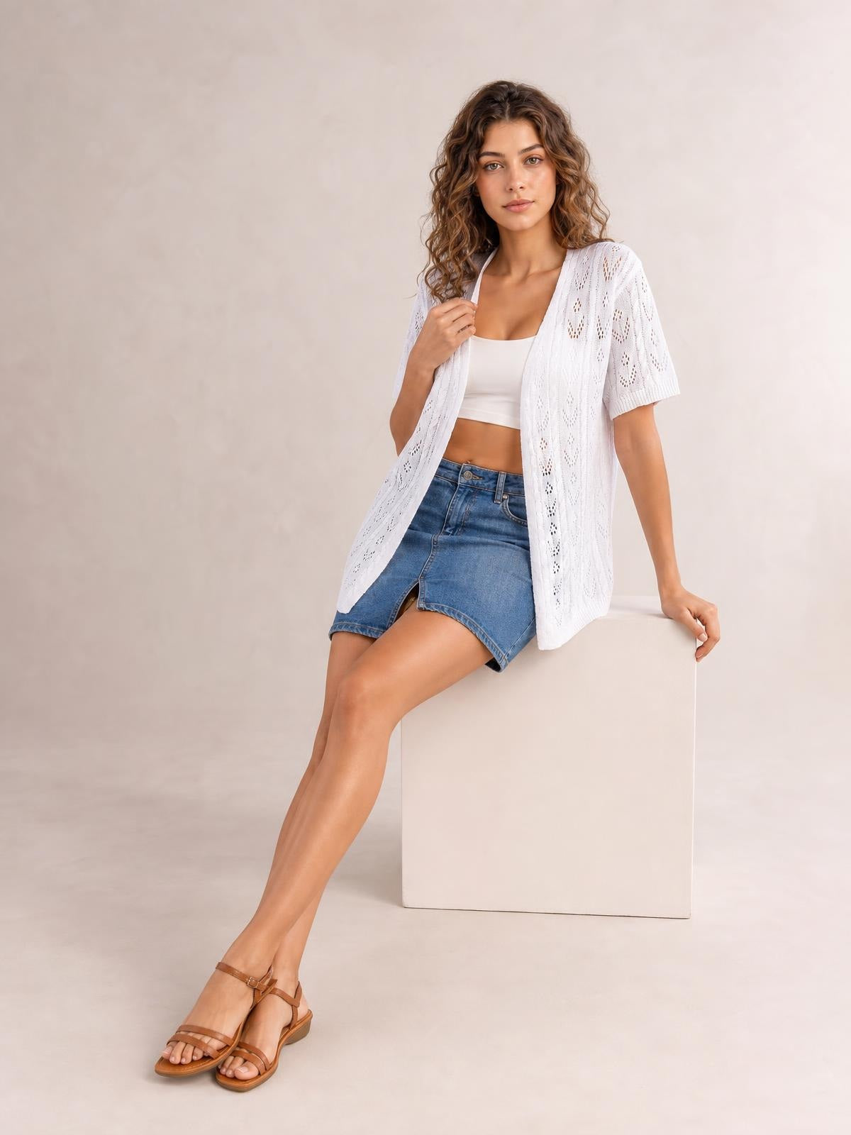 Model wears a white openwork open-front cardigan with short half sleeves and a relaxed longline silhouette over a crop top and denim shorts.