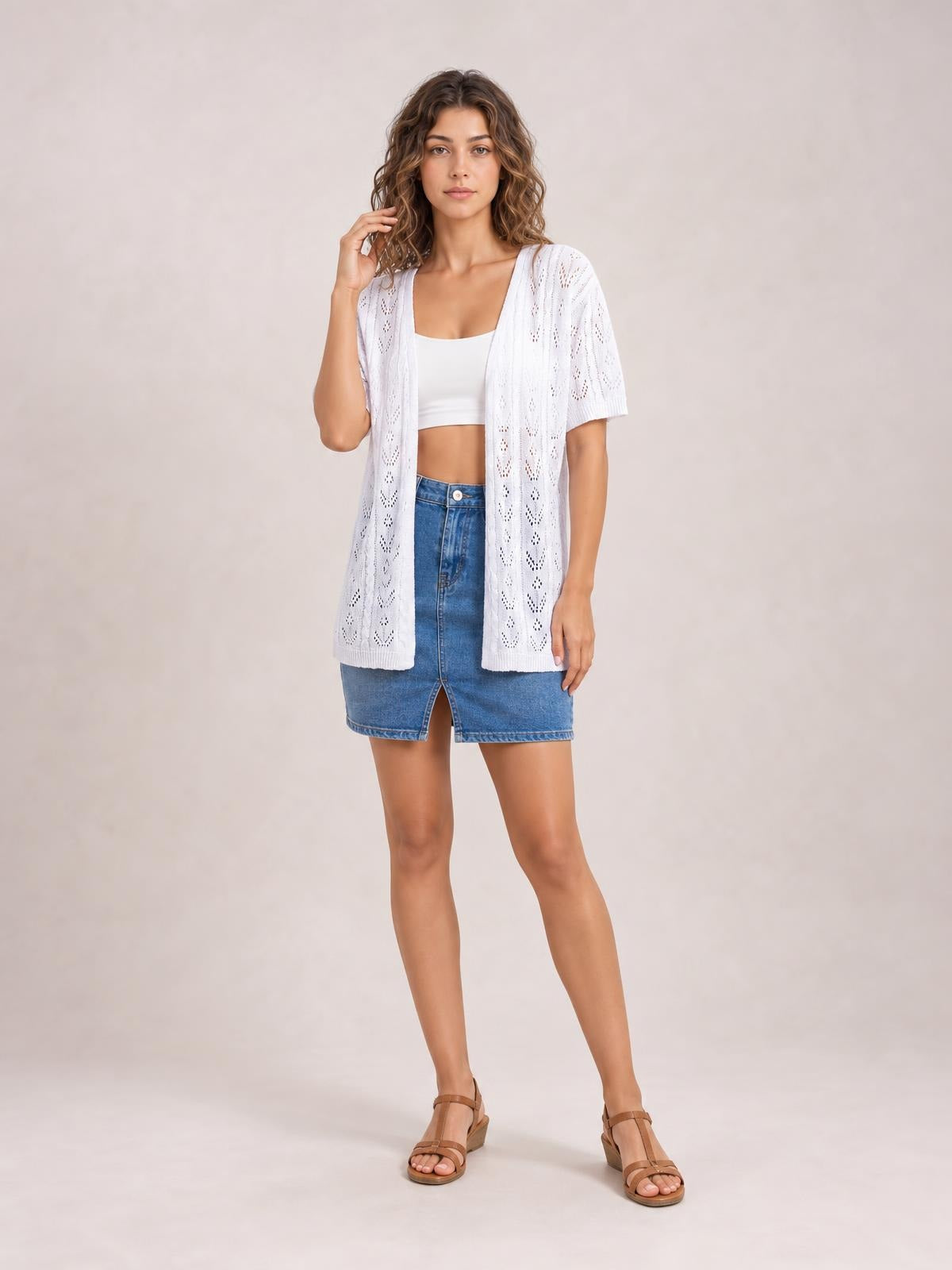Model wearing a white openwork open-front half-sleeve cardigan with a relaxed hip-length silhouette over a cropped top, posing with one hand near her hair.