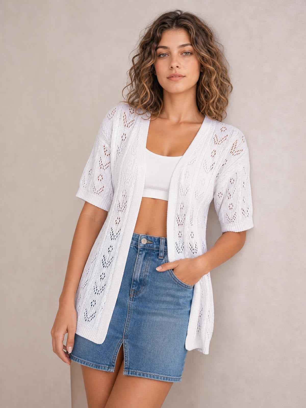 A model poses in a white openwork open-front cardigan with half sleeves and a relaxed long silhouette, layered over a white crop top.