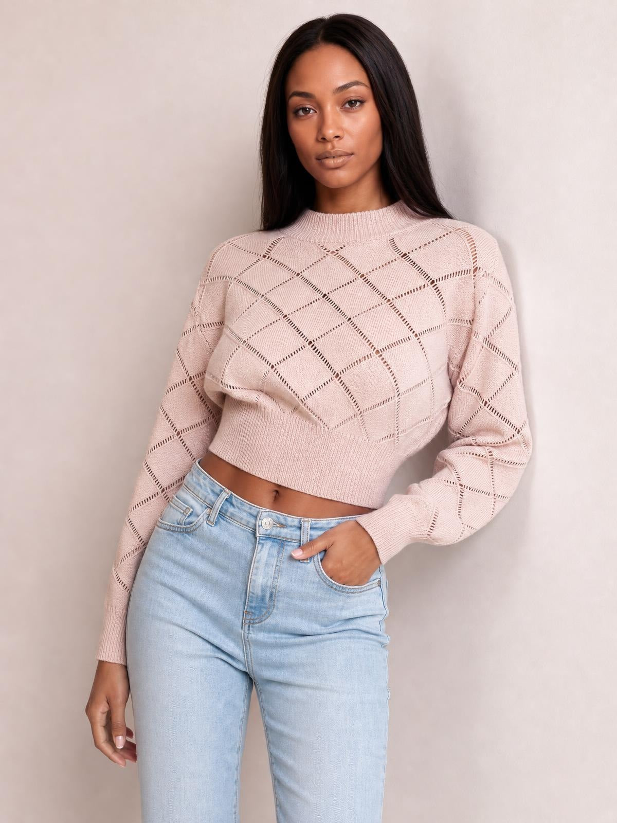 Model wearing a blush pink cropped sweater with an openwork plaid knit, round neckline, long sleeves, ribbed cuffs, and a fitted ribbed hem.
